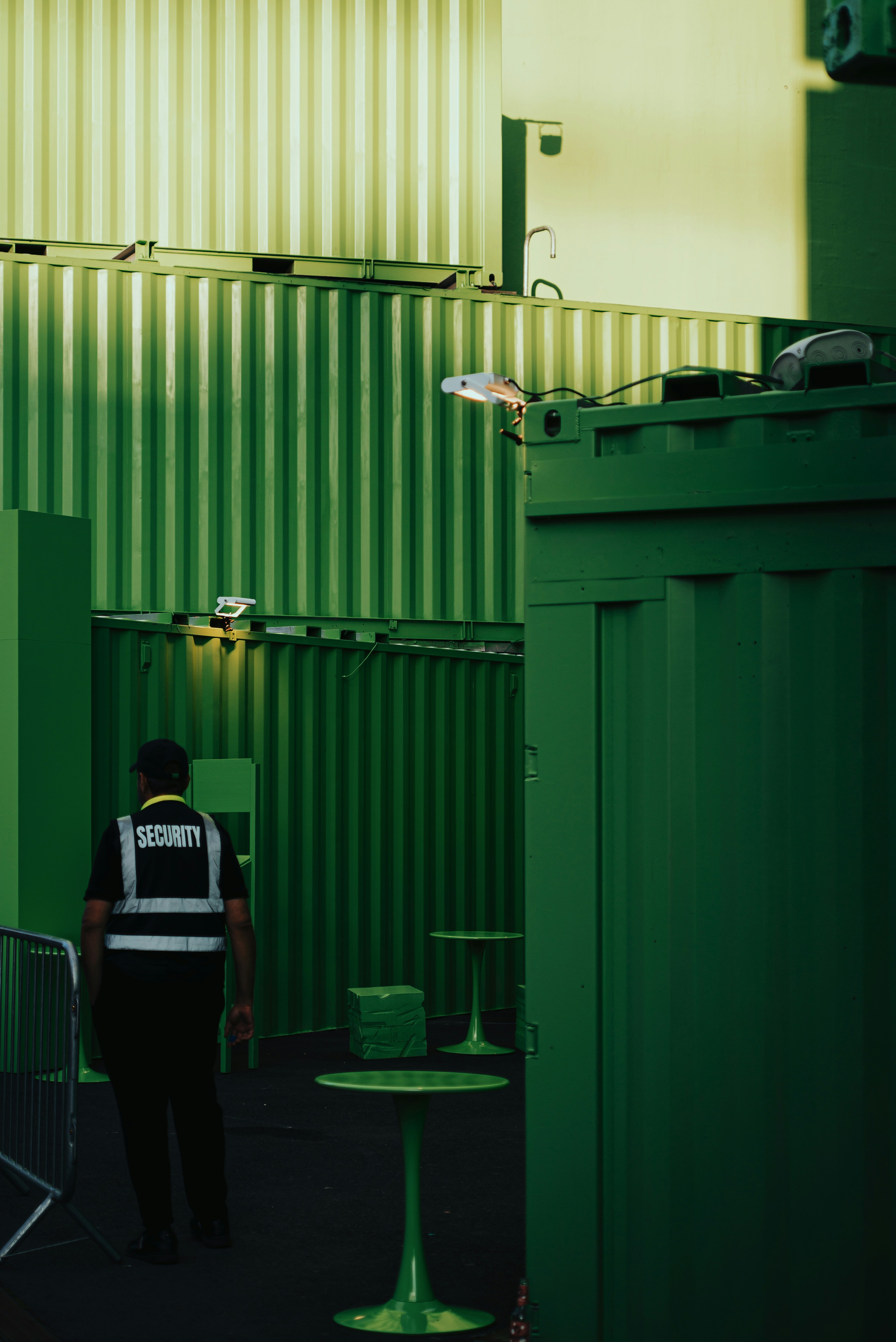 A security guard in a reflective vest walking past green shipping containers in Berlin