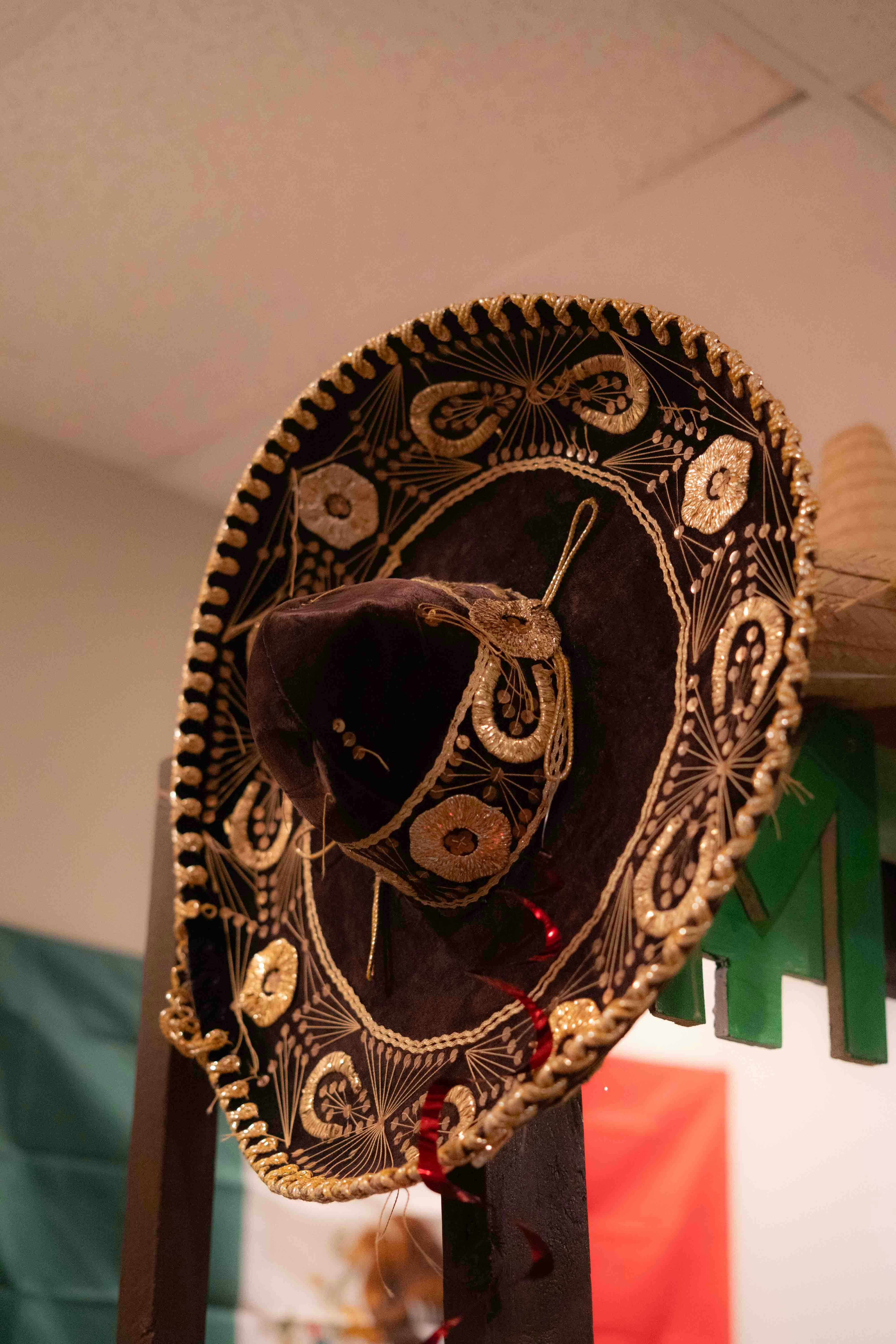 A dark brown sombrero with intricate gold embroidery hanging on a wooden stand