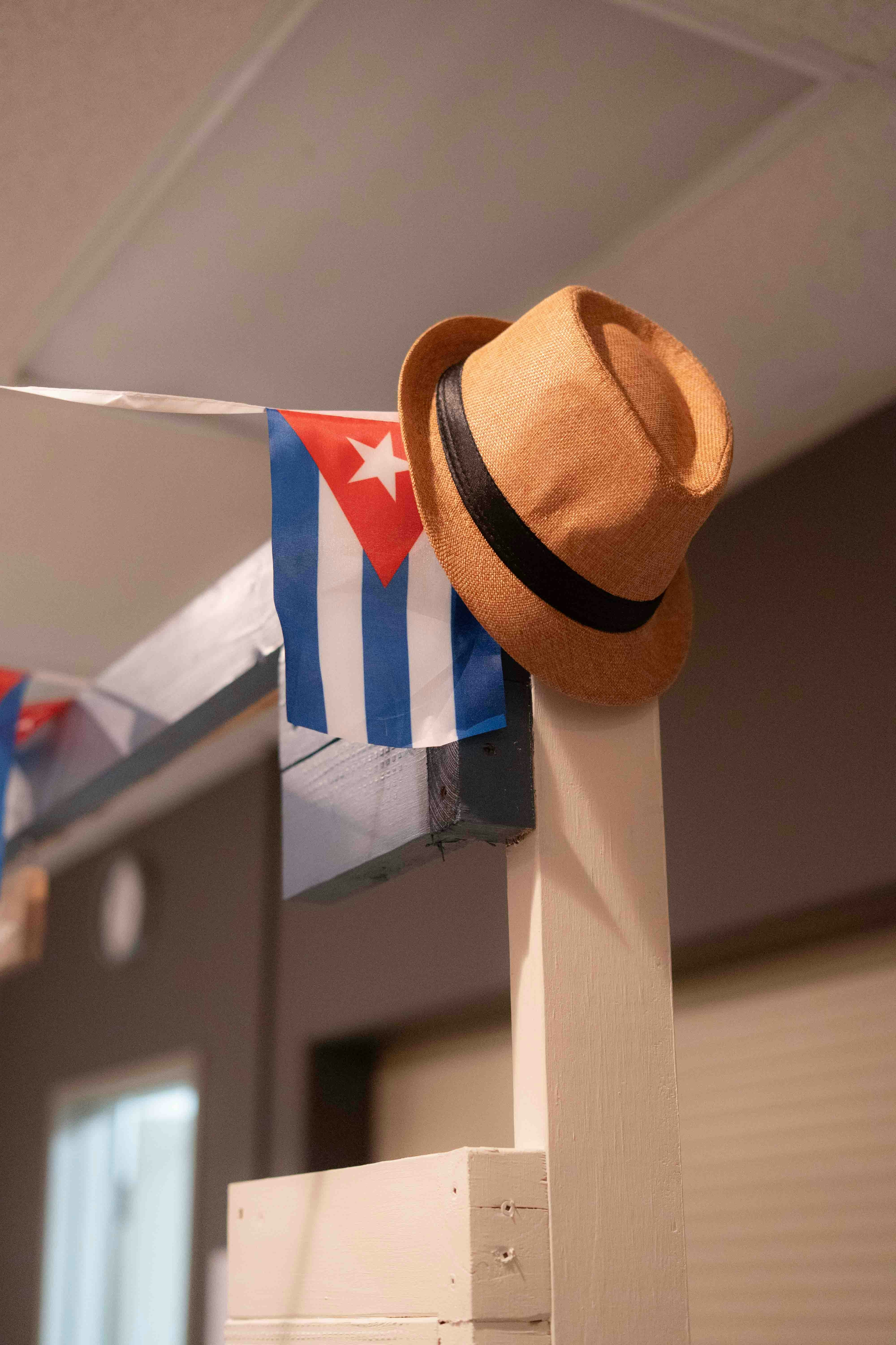 A straw fedora hat resting on a wooden post beside a Cuban flag