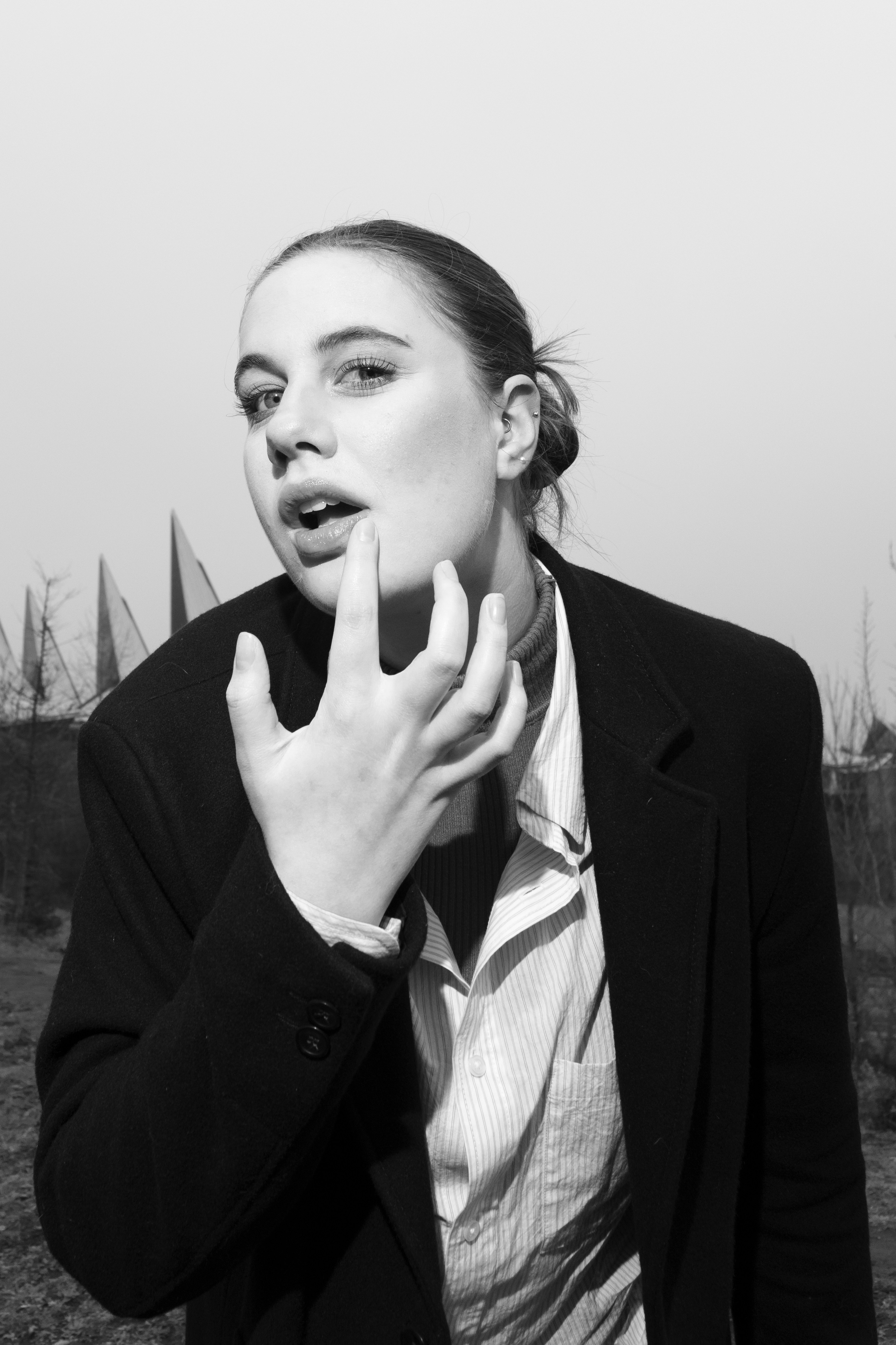 A woman in a black coat and striped shirt touching her lip outdoors