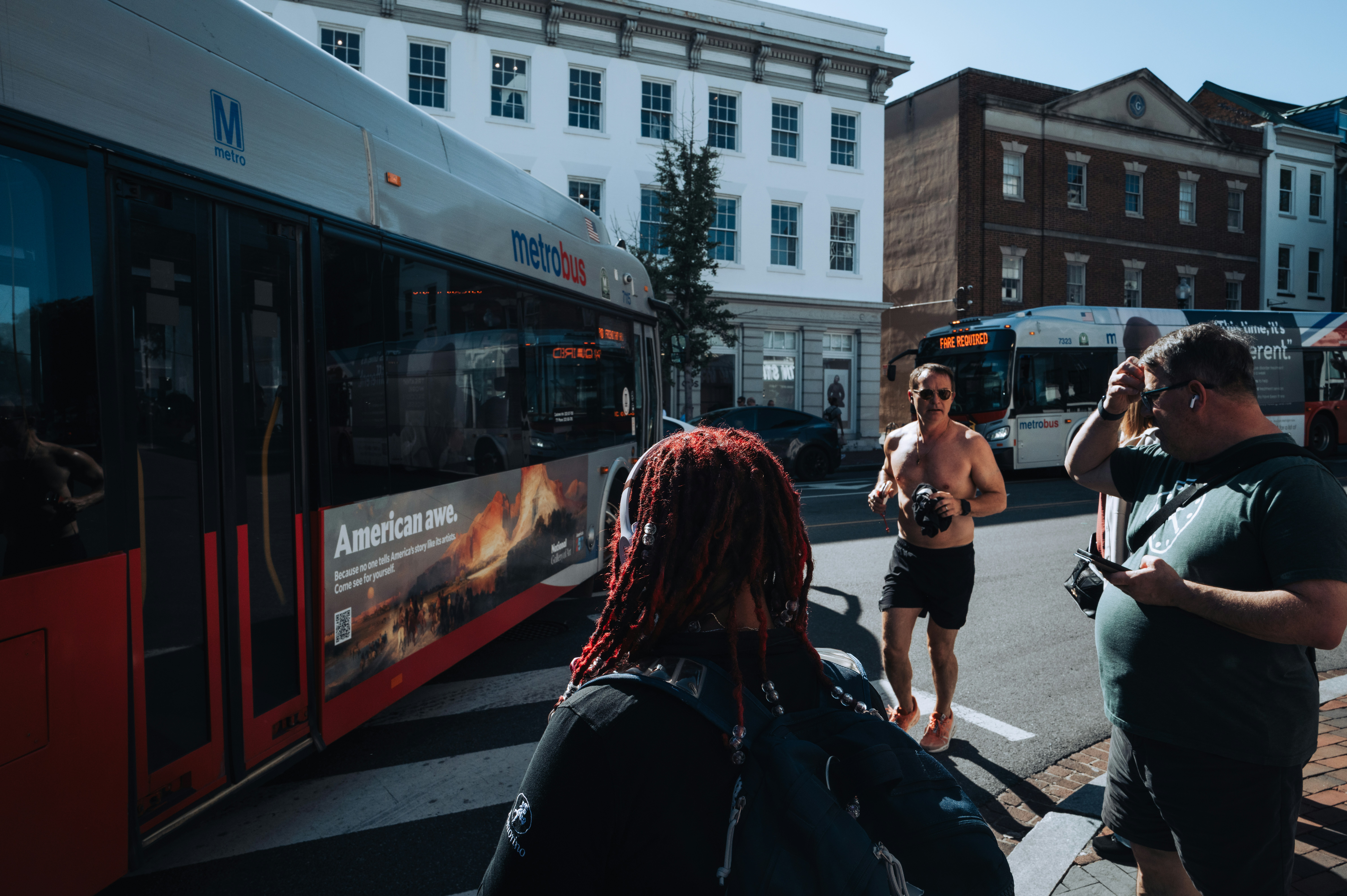 People on a city street near a metrobus with an advertisement on its side