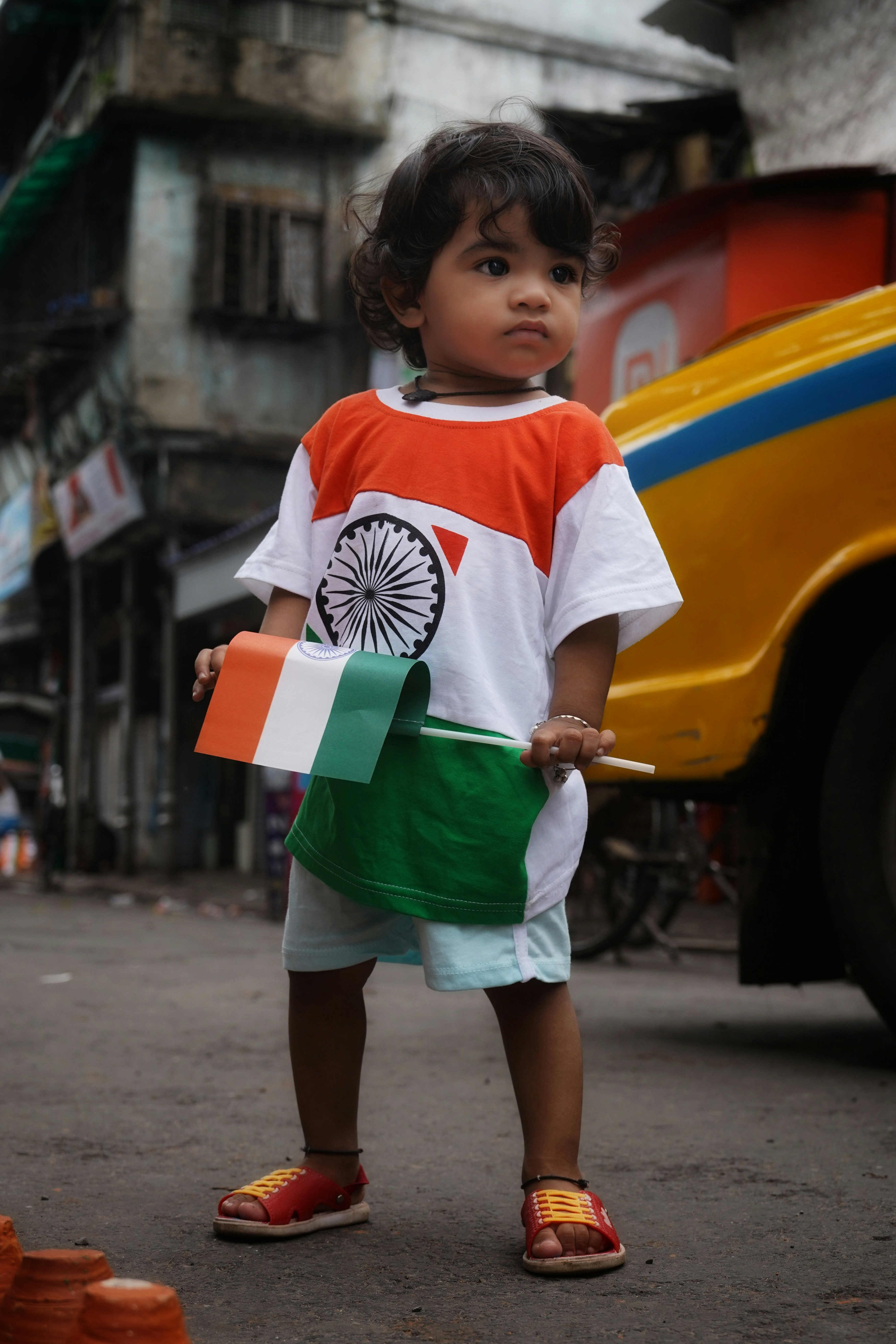 A toddler wearing a shirt with the Indian flag design holding a small flag