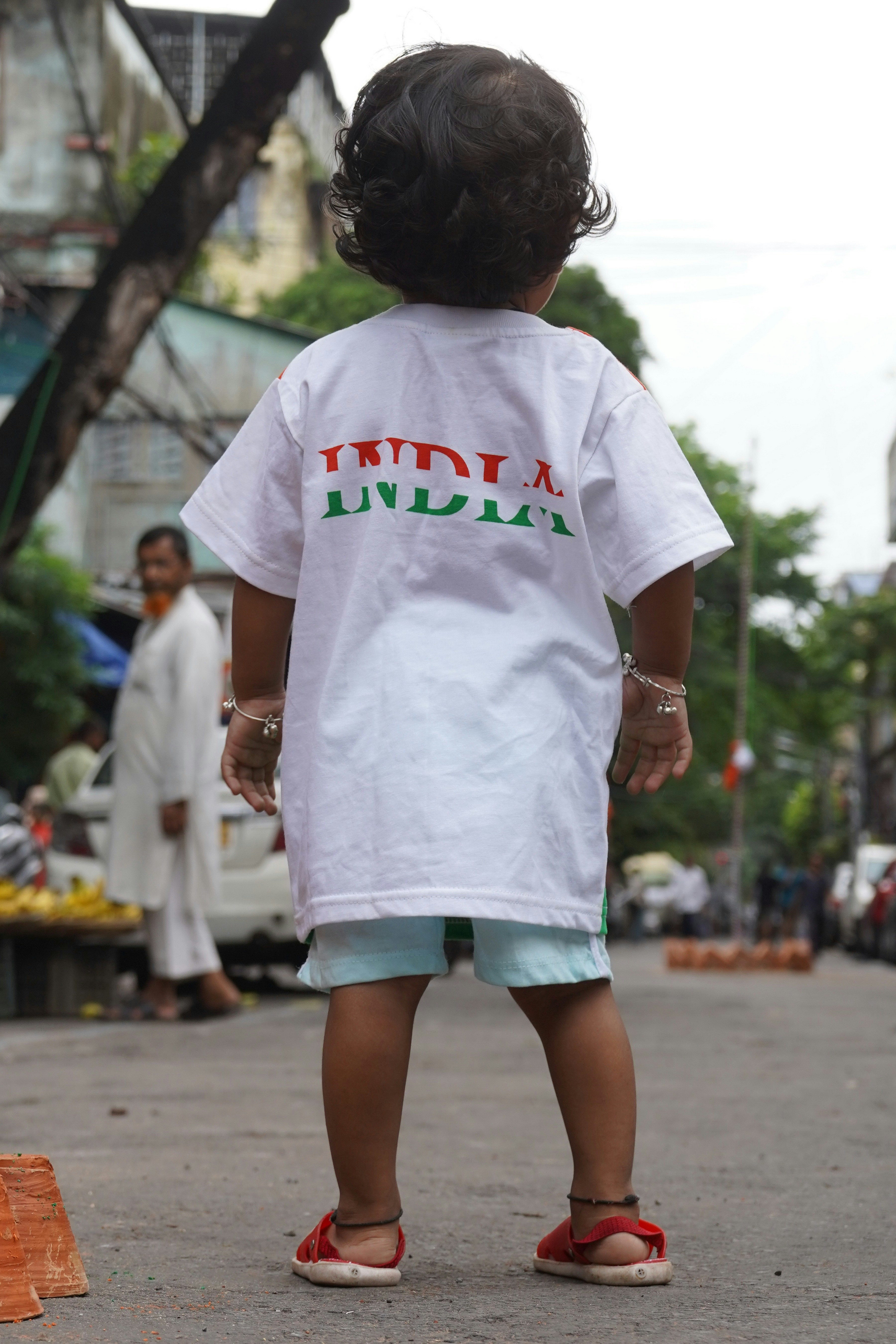 A child in a white t-shirt reading India on a city street