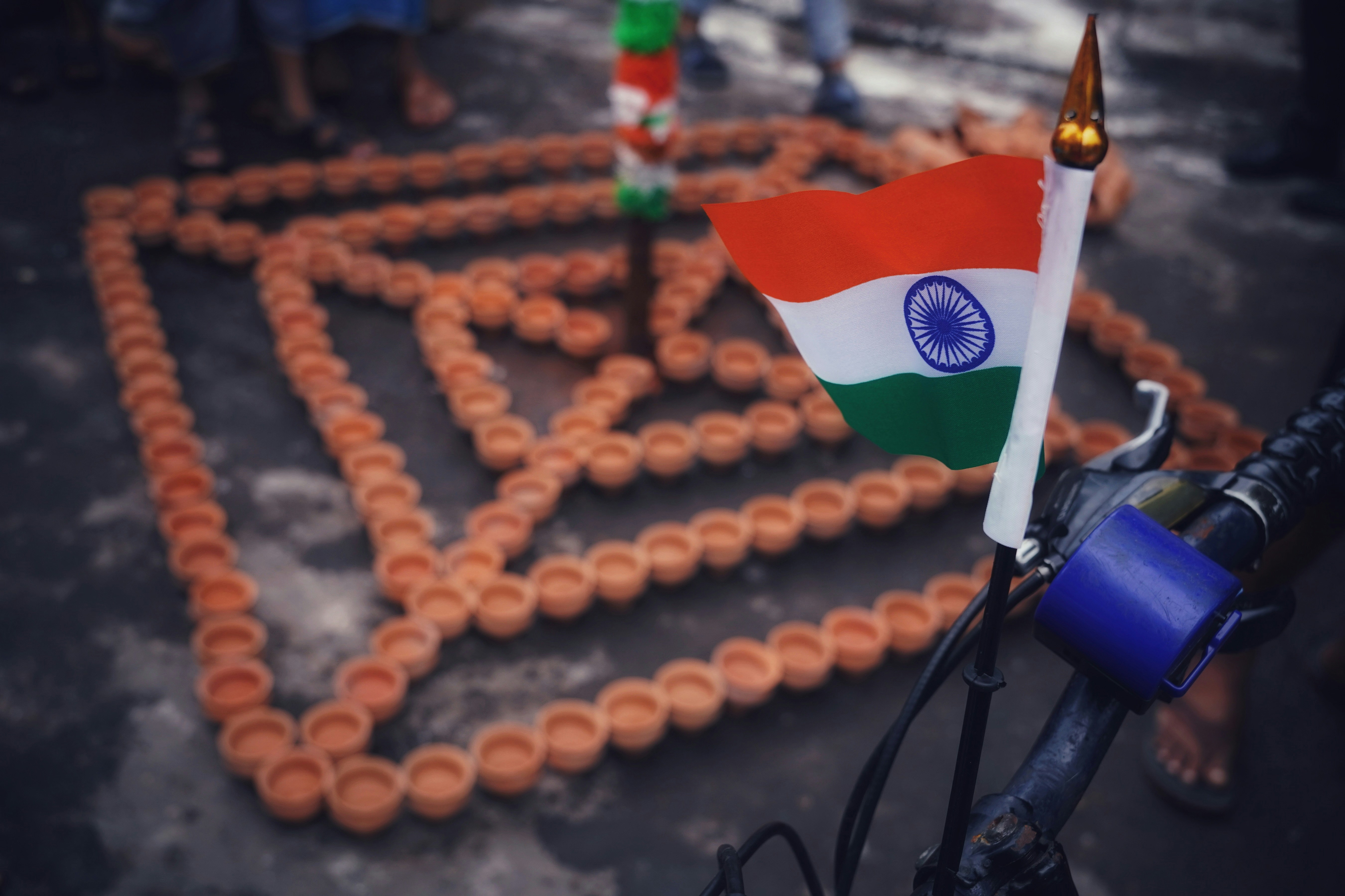 The Indian flag attached to a bicycle near a geometric pattern of clay lamps