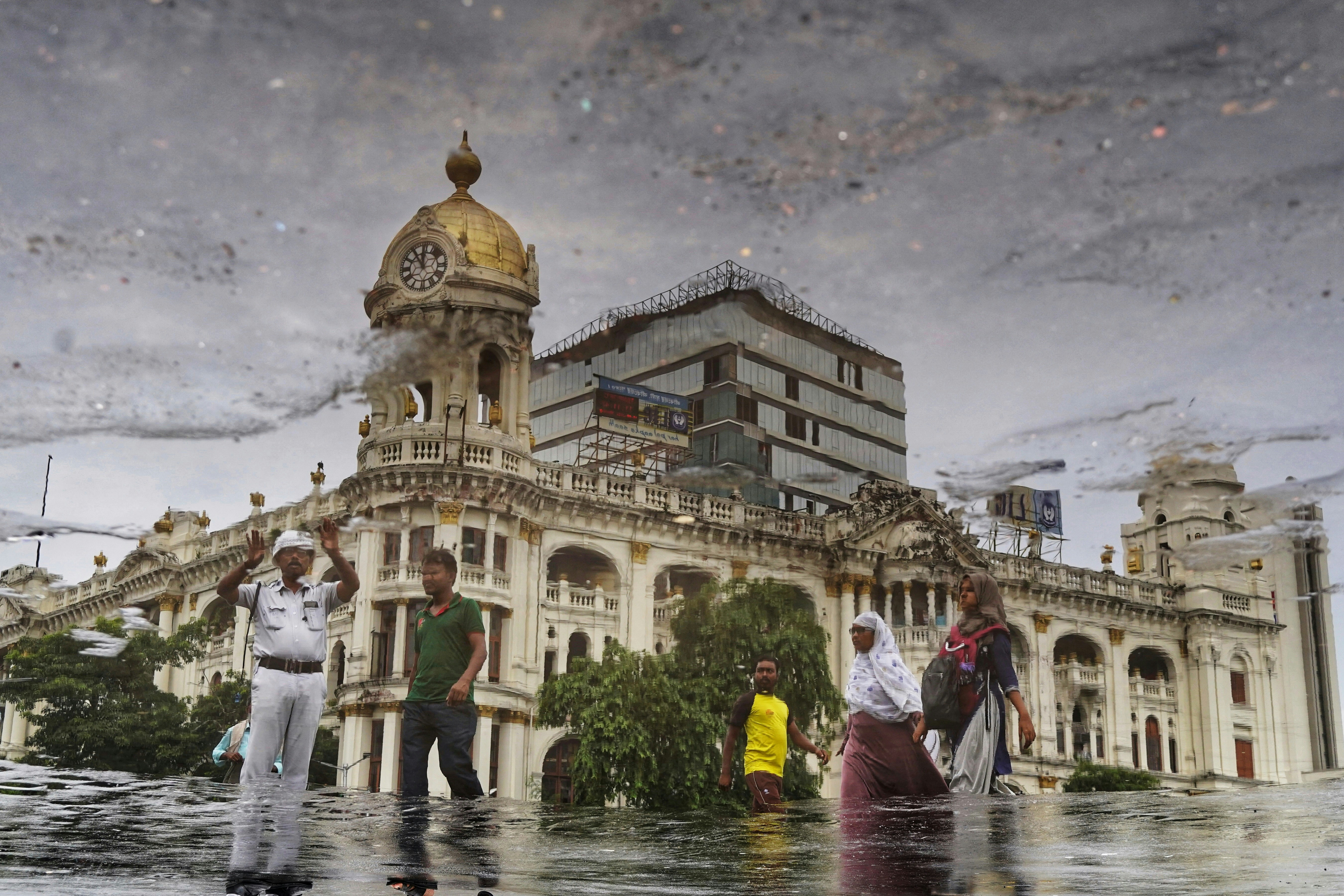 People walking through a flooded street reflecting the Esplanade Mansions in Kolkata