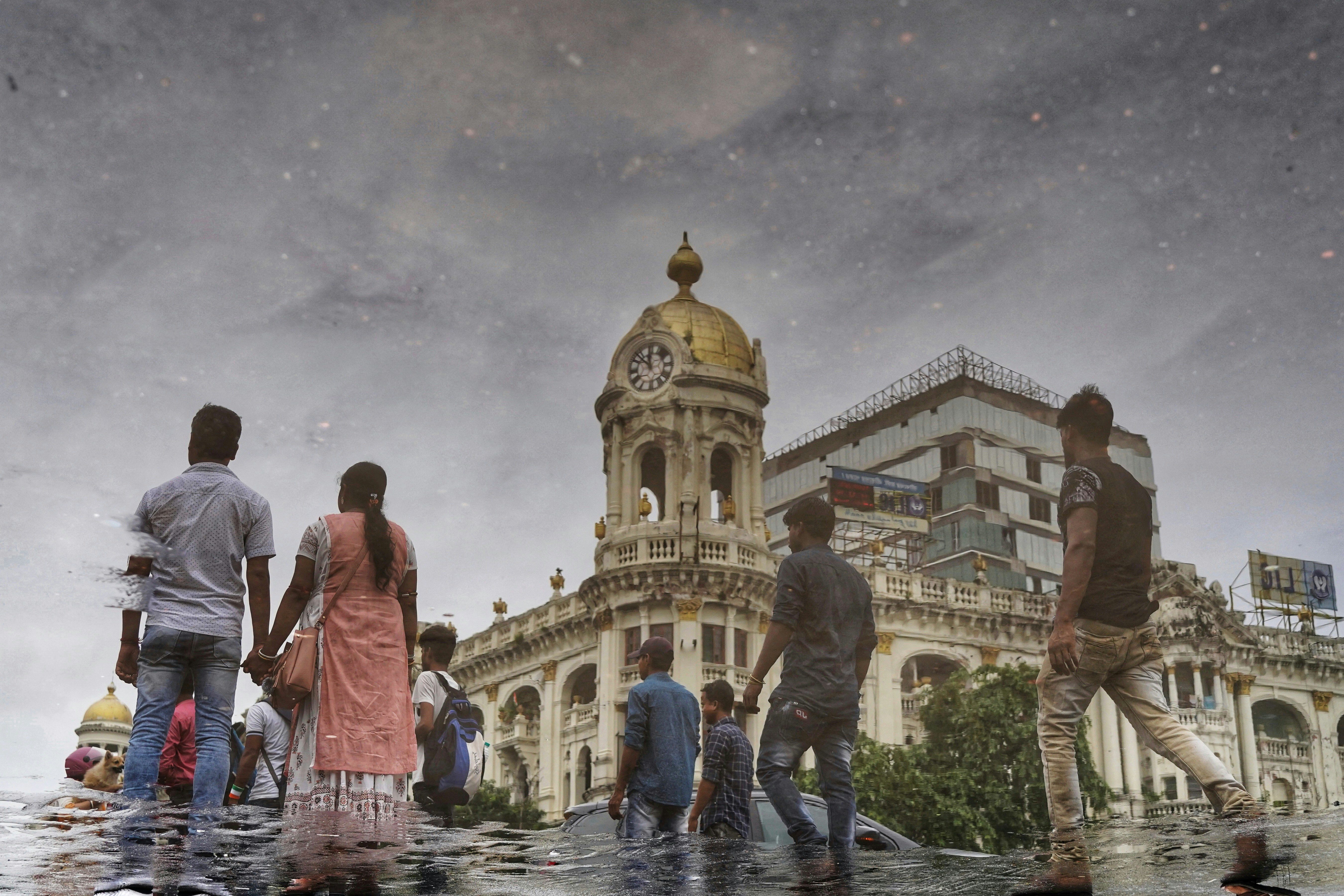 People walking through a flooded street reflecting the Esplanade Mansions in Kolkata