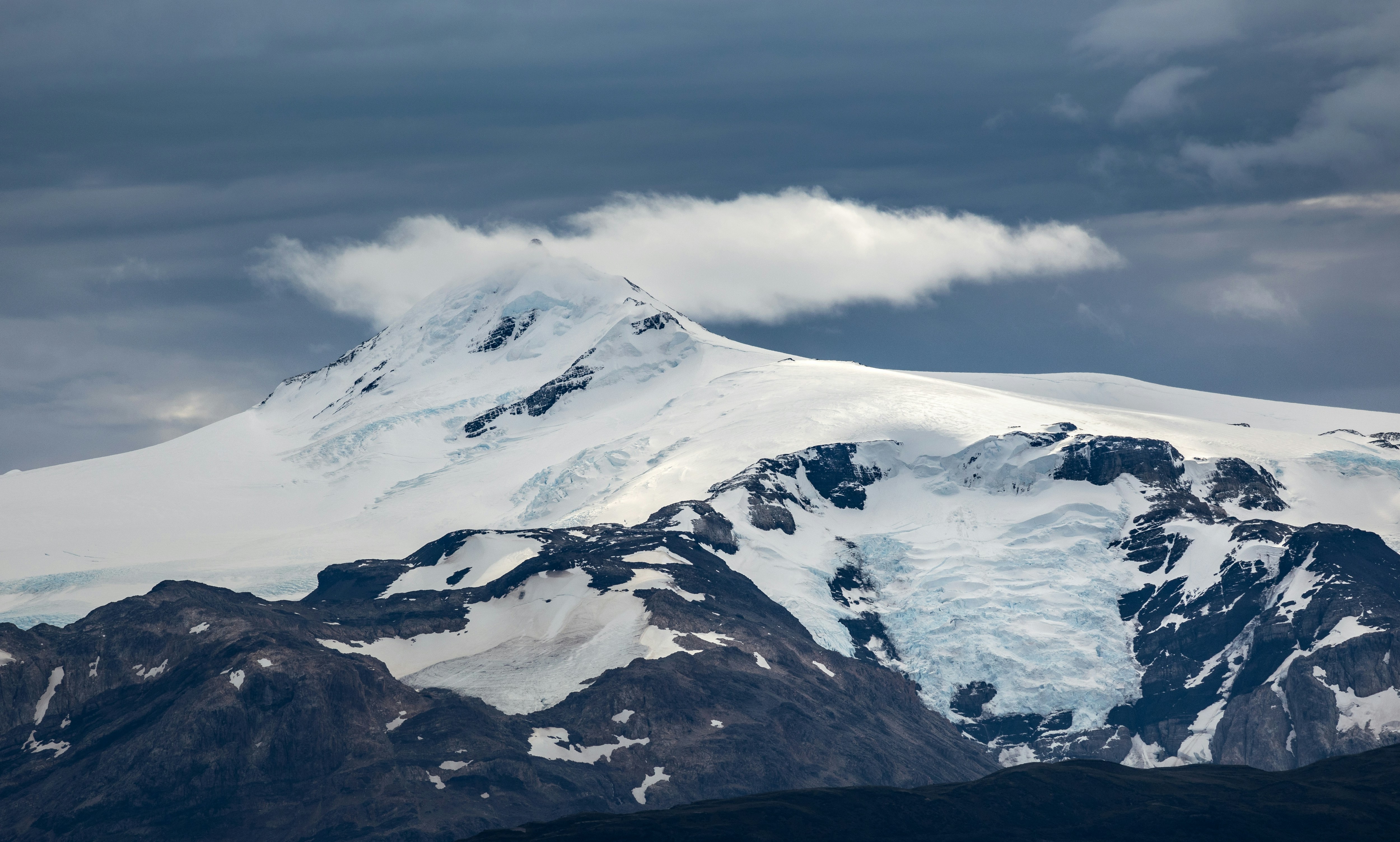 A snow-covered mountain peak with a small cloud under a dark sky