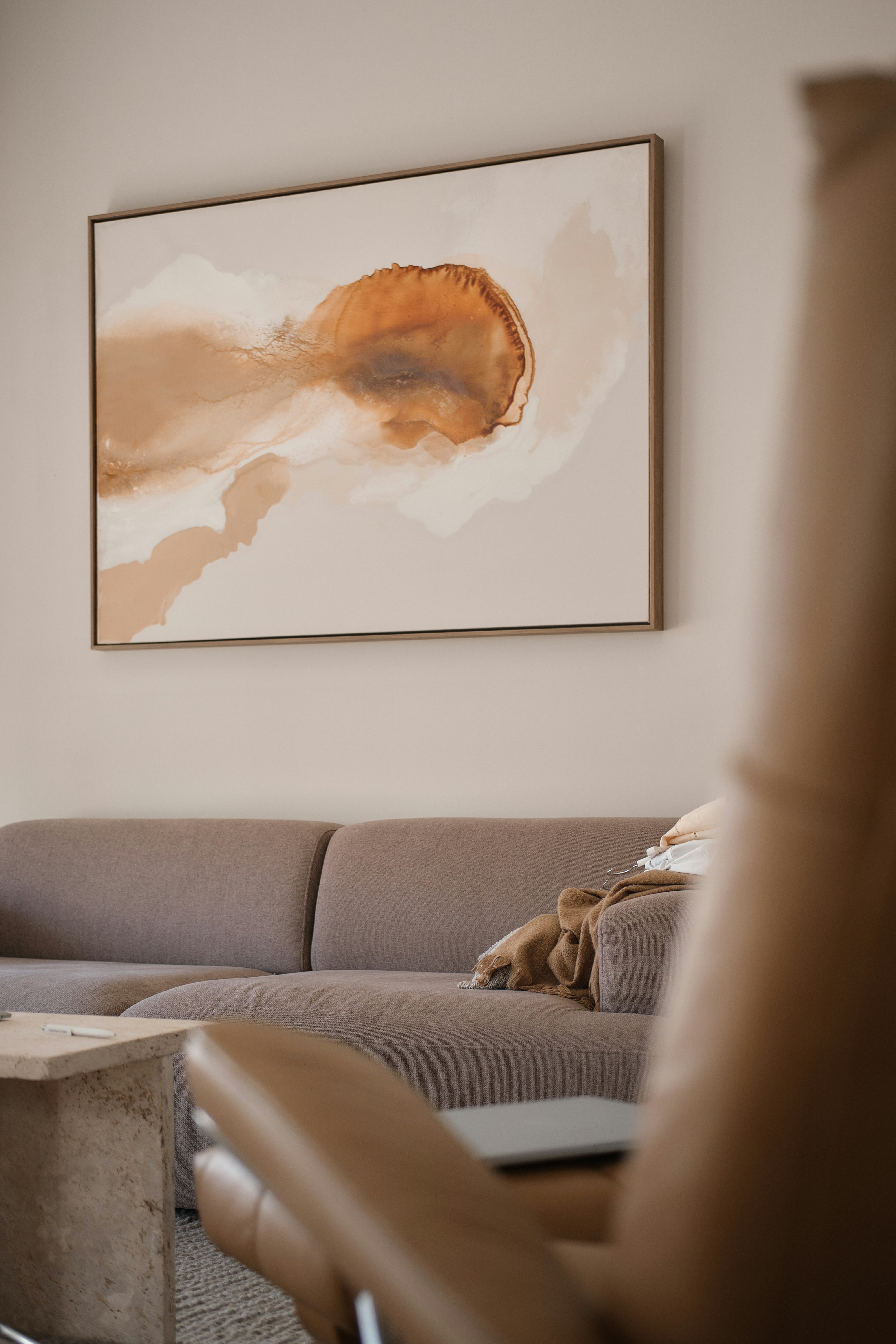 A brown sofa with a throw blanket below an abstract painting in a living room