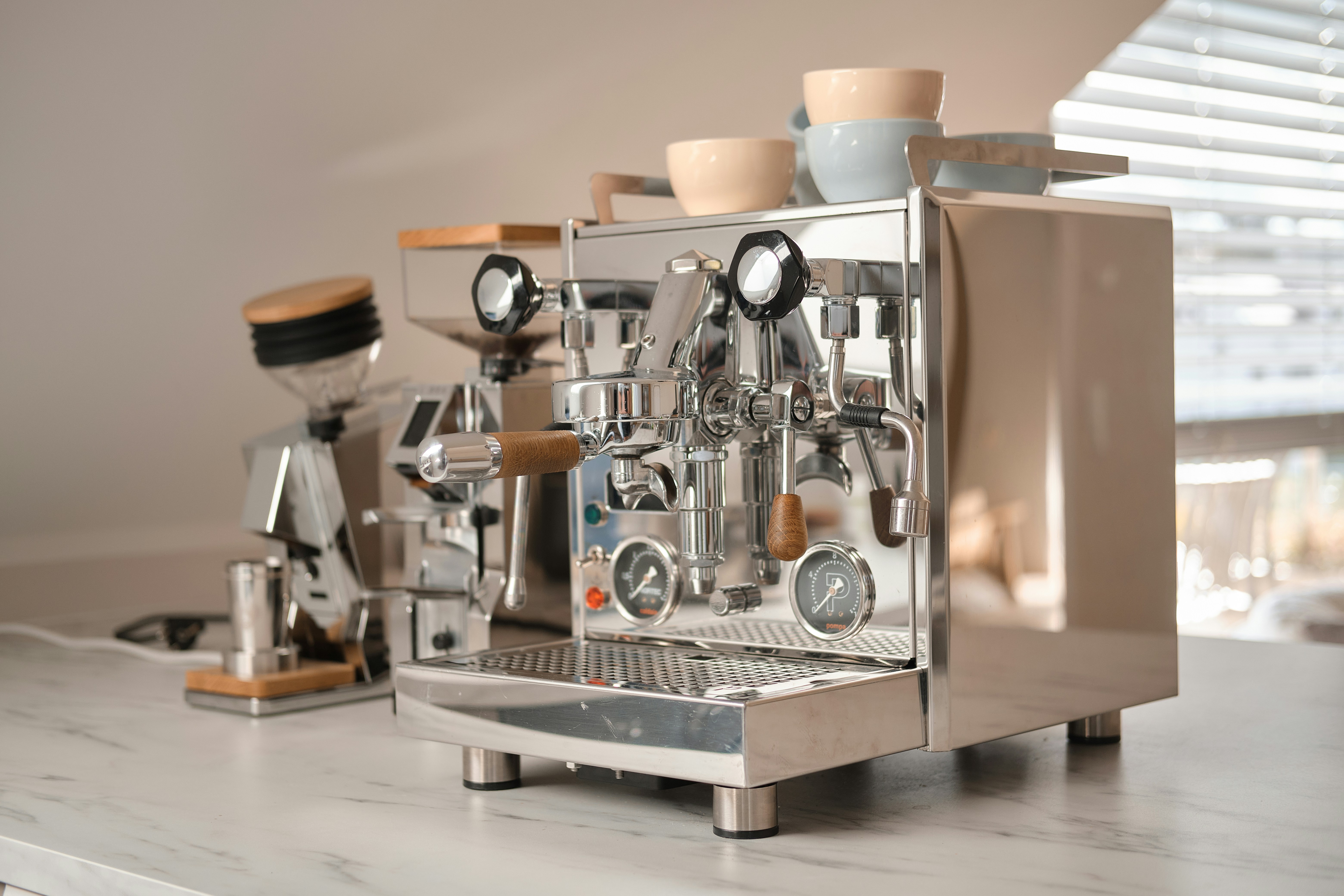 A chrome espresso machine and coffee grinder on a white marble countertop