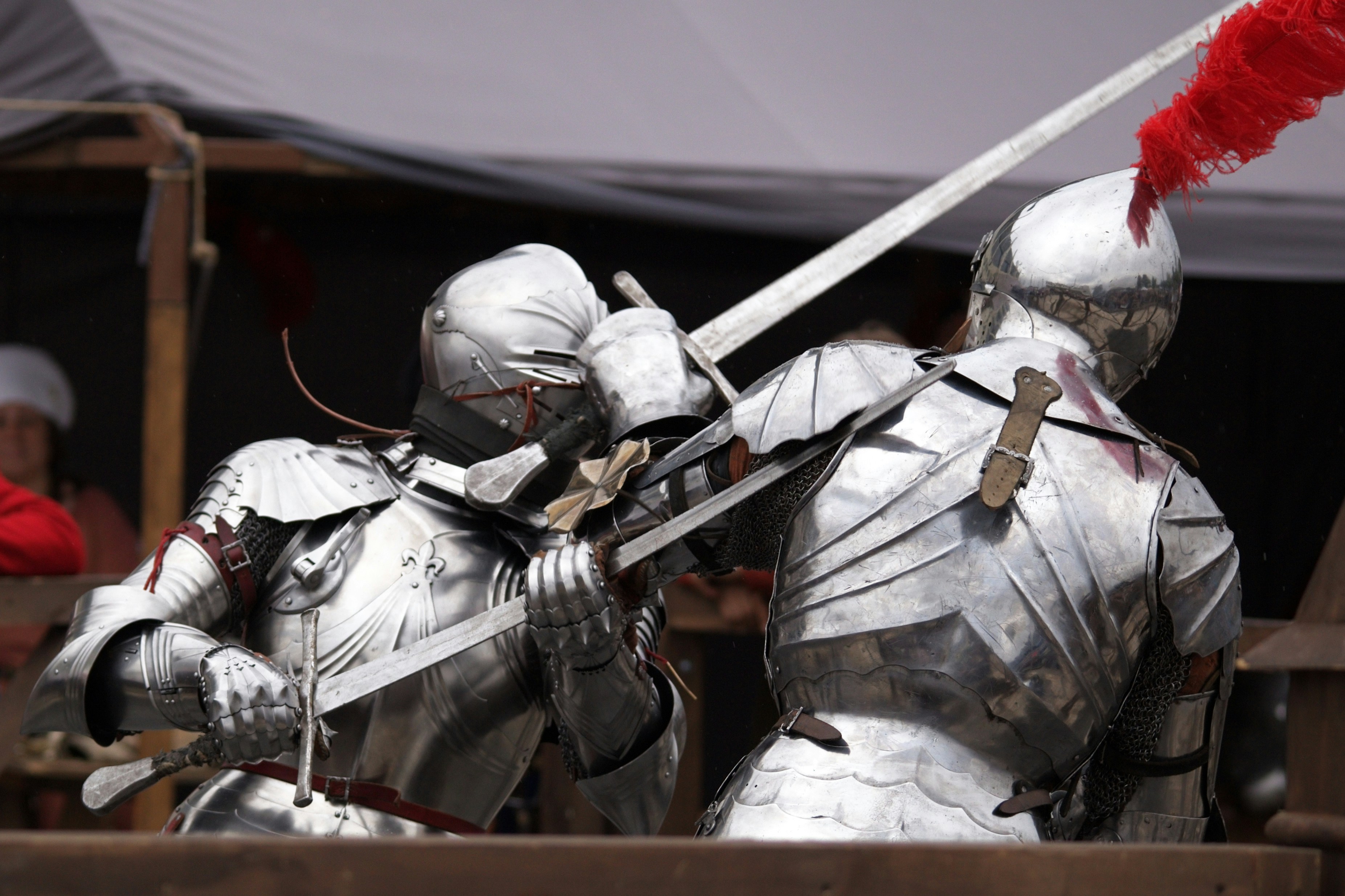 Two knights in polished steel plate armor dueling with swords at a tournament
