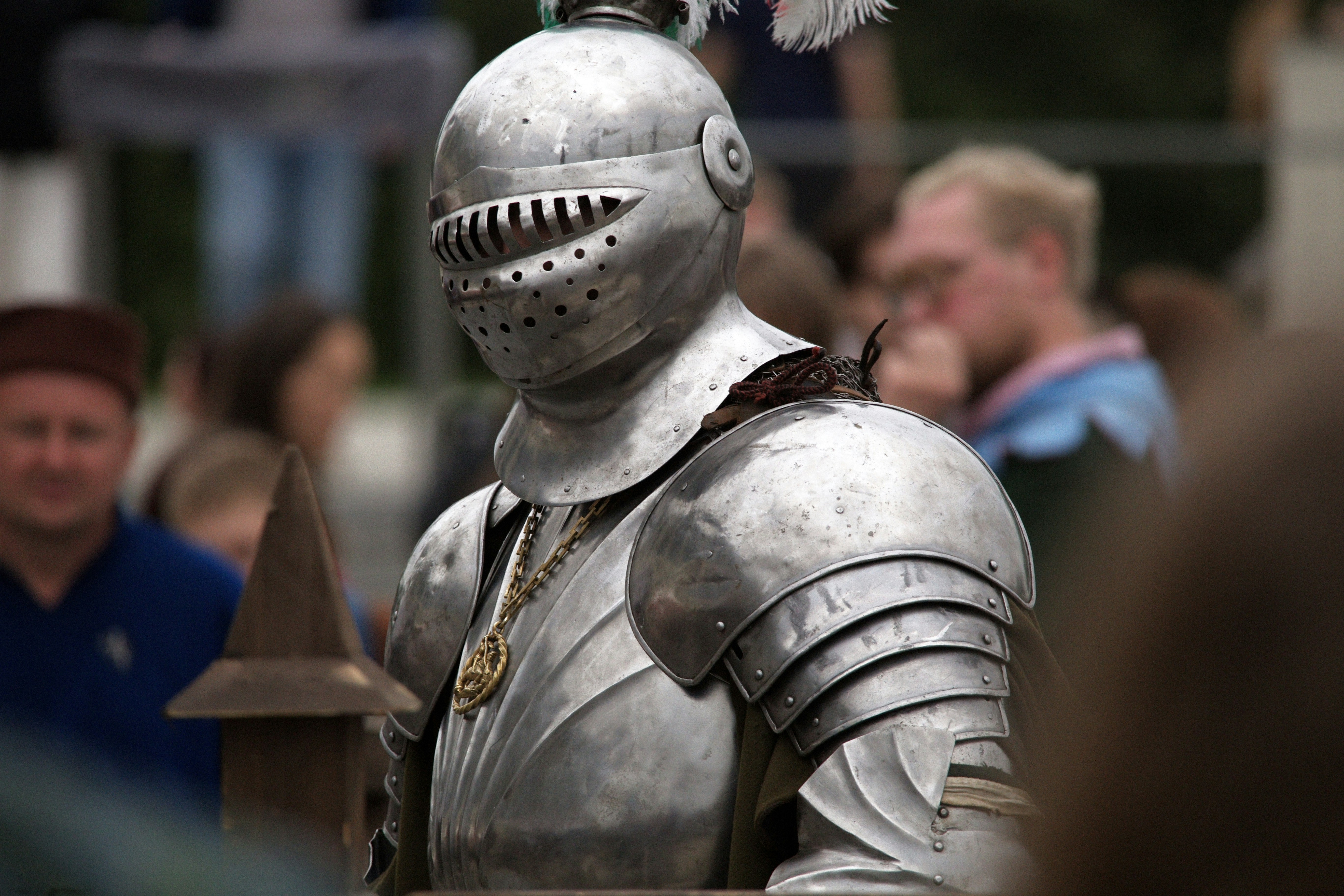 A person in polished steel plate armor with a helmet at a public event