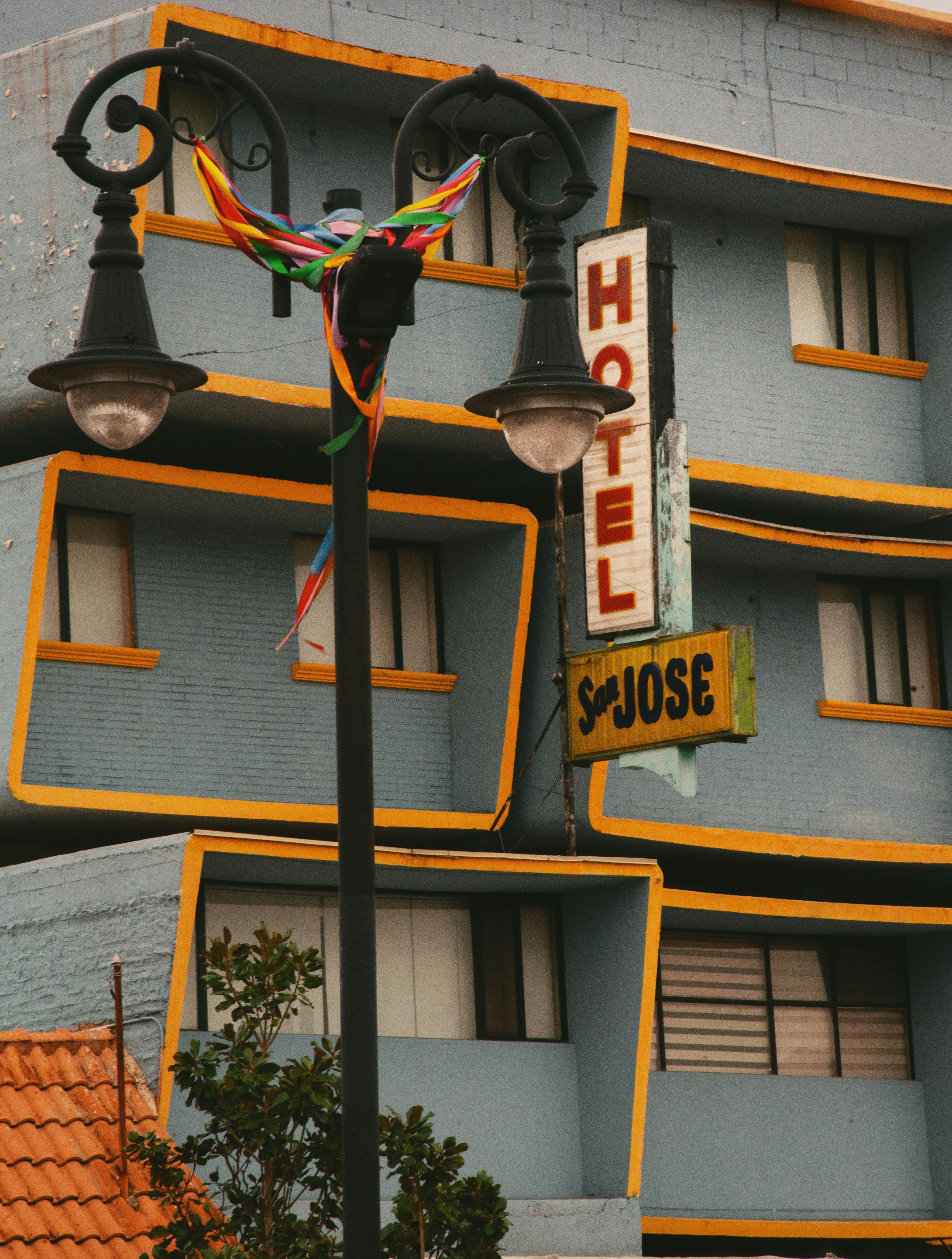 A street lamp with colorful ribbons before a blue hotel with yellow trim