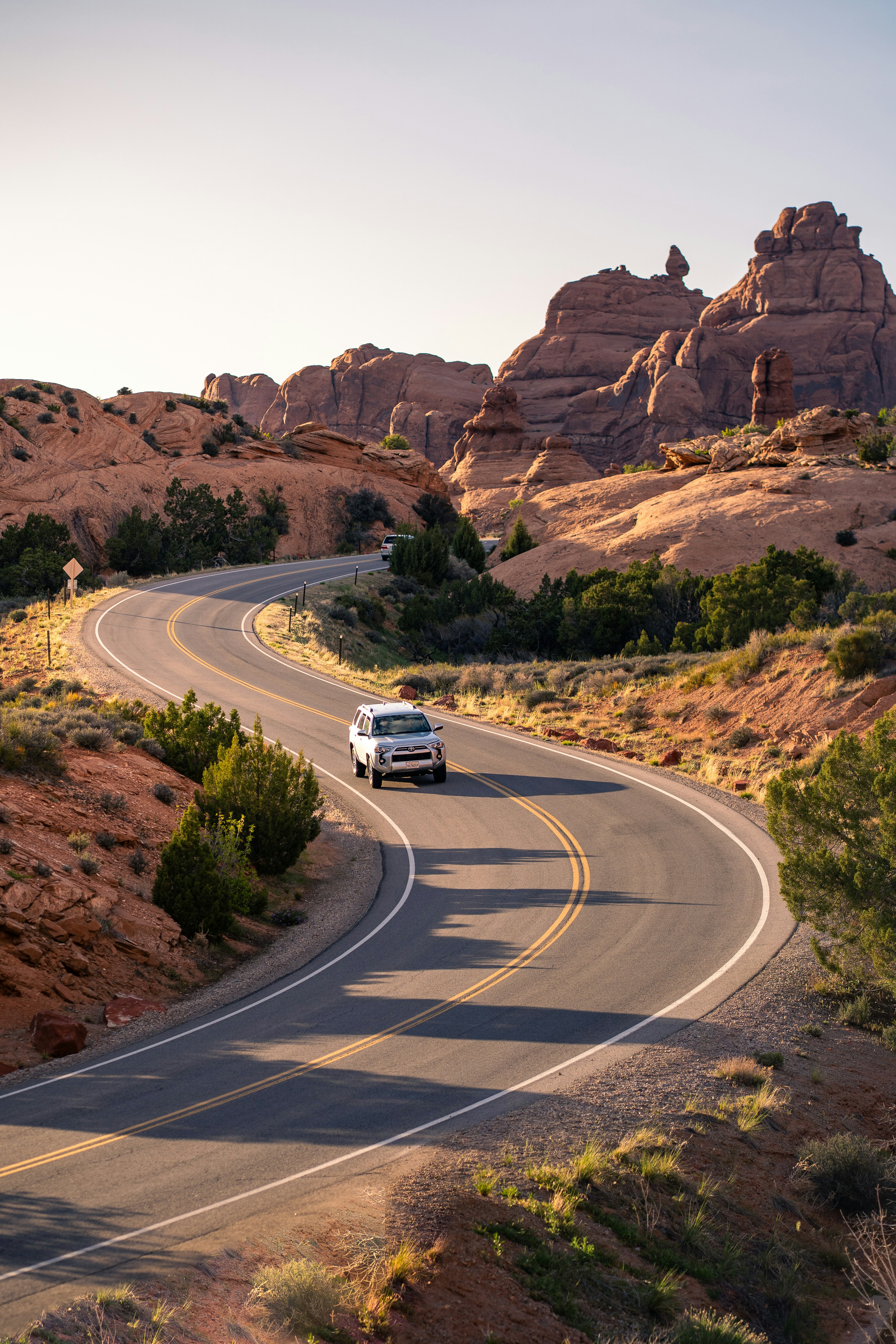 A silver SUV driving on a winding road through a red rock desert landscape