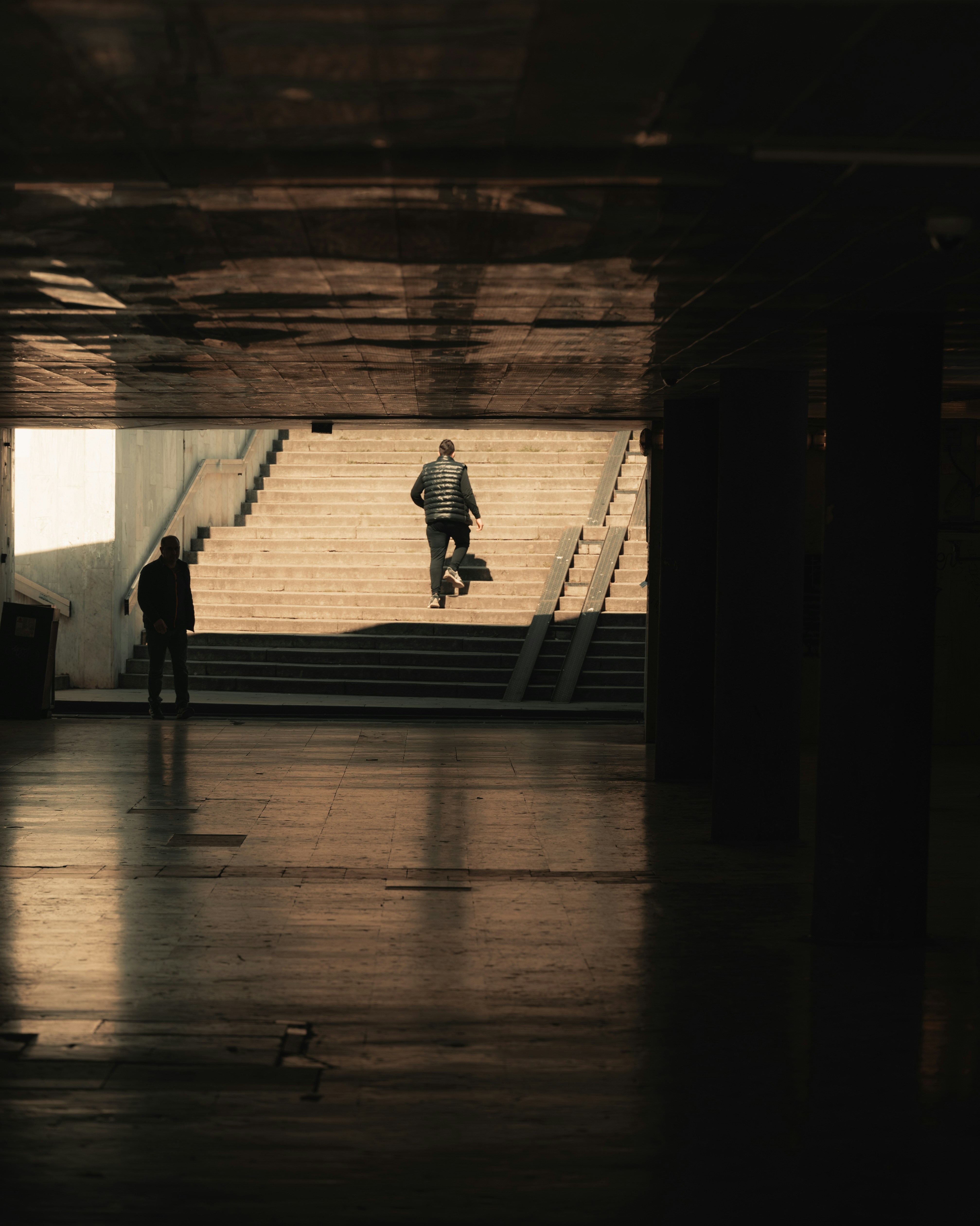 A person walking up concrete stairs in a dark tunnel toward bright light
