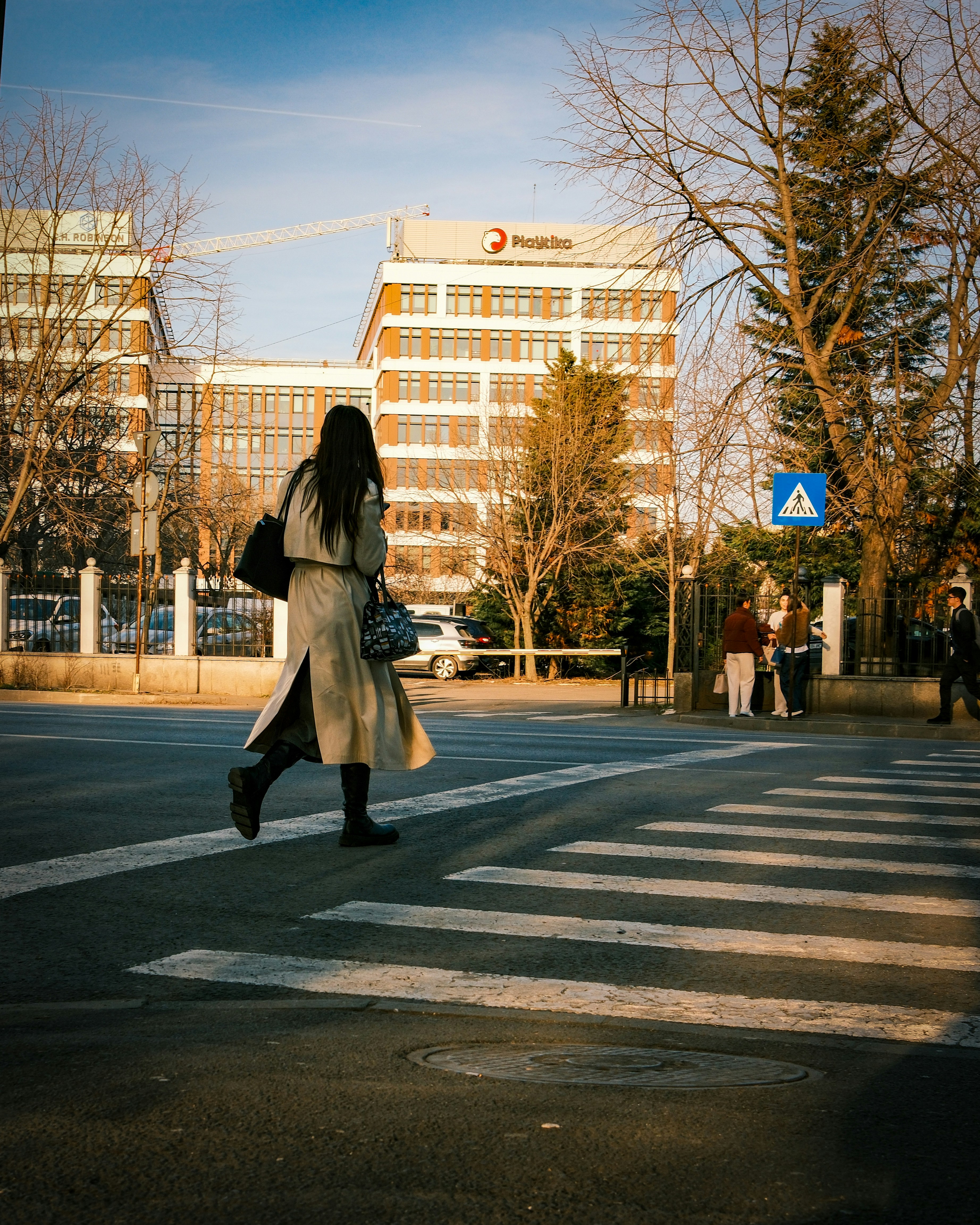 A woman in a long beige coat crossing a street on a crosswalk