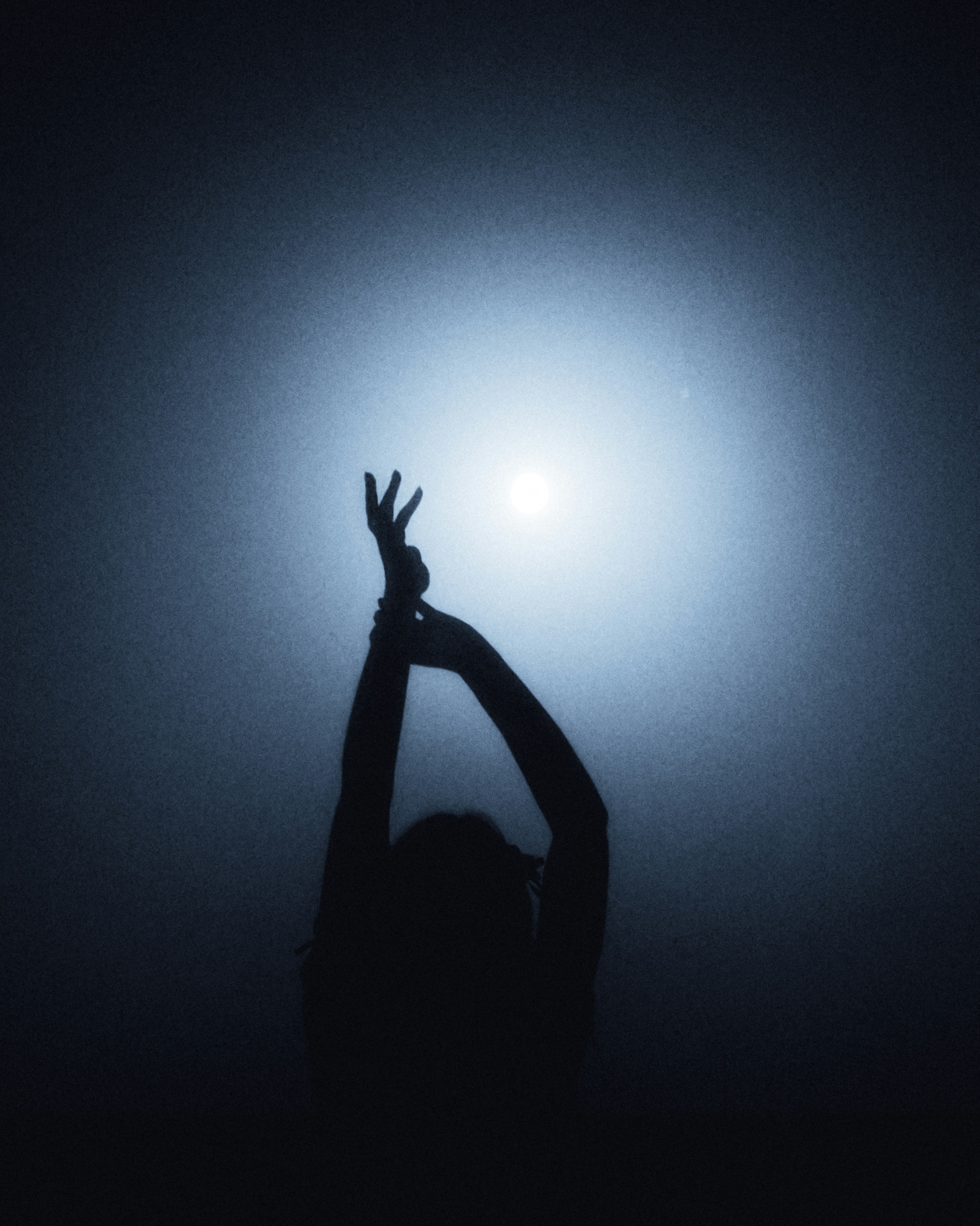 A person in silhouette with arms raised against a bright blue light
