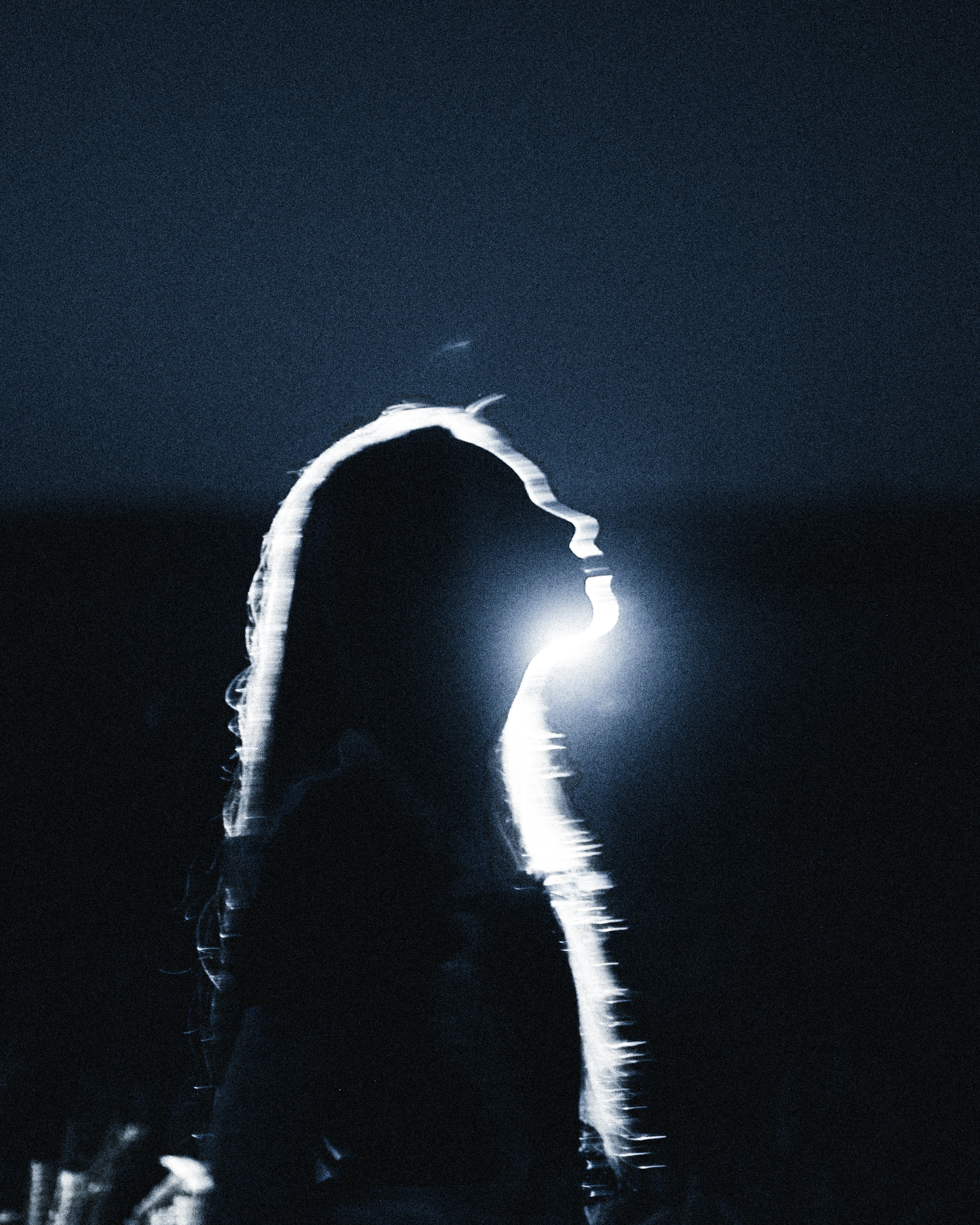 A silhouette of a person with long hair against a bright light source