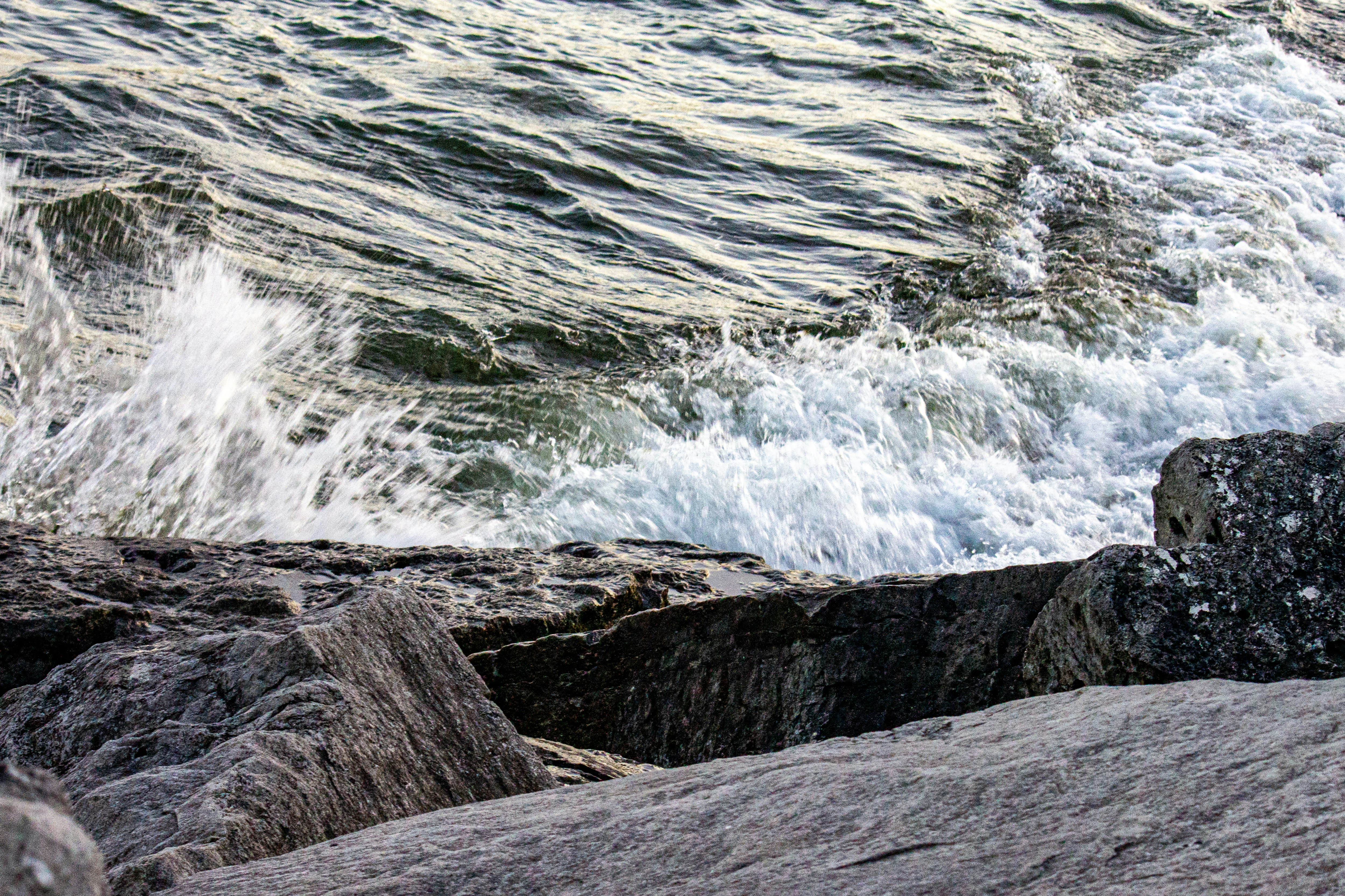 White sea foam crashing against dark grey rocks along a shoreline