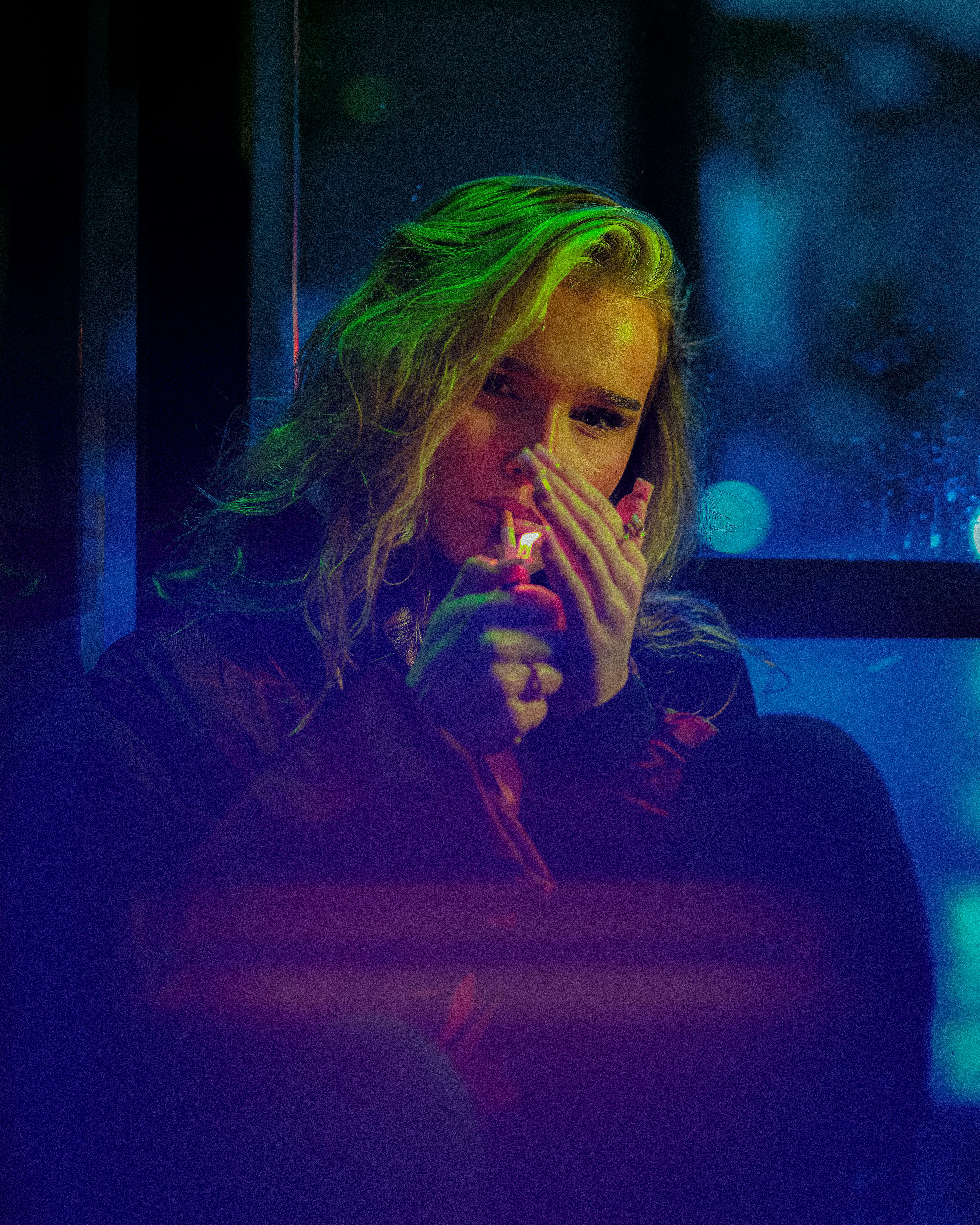 A woman lighting a cigarette with a lighter in blue and green neon light