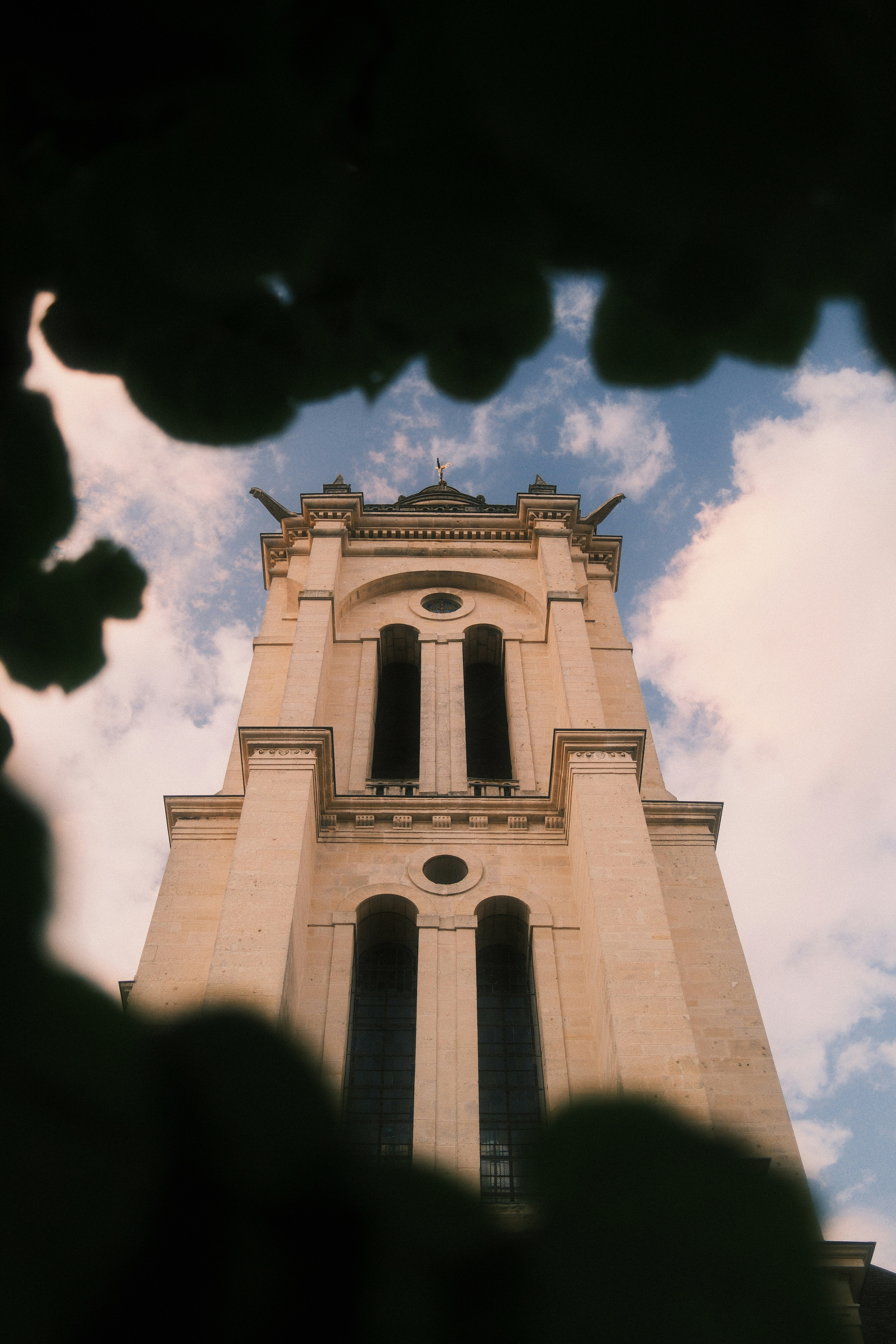 A stone church tower framed by dark foliage against a blue sky