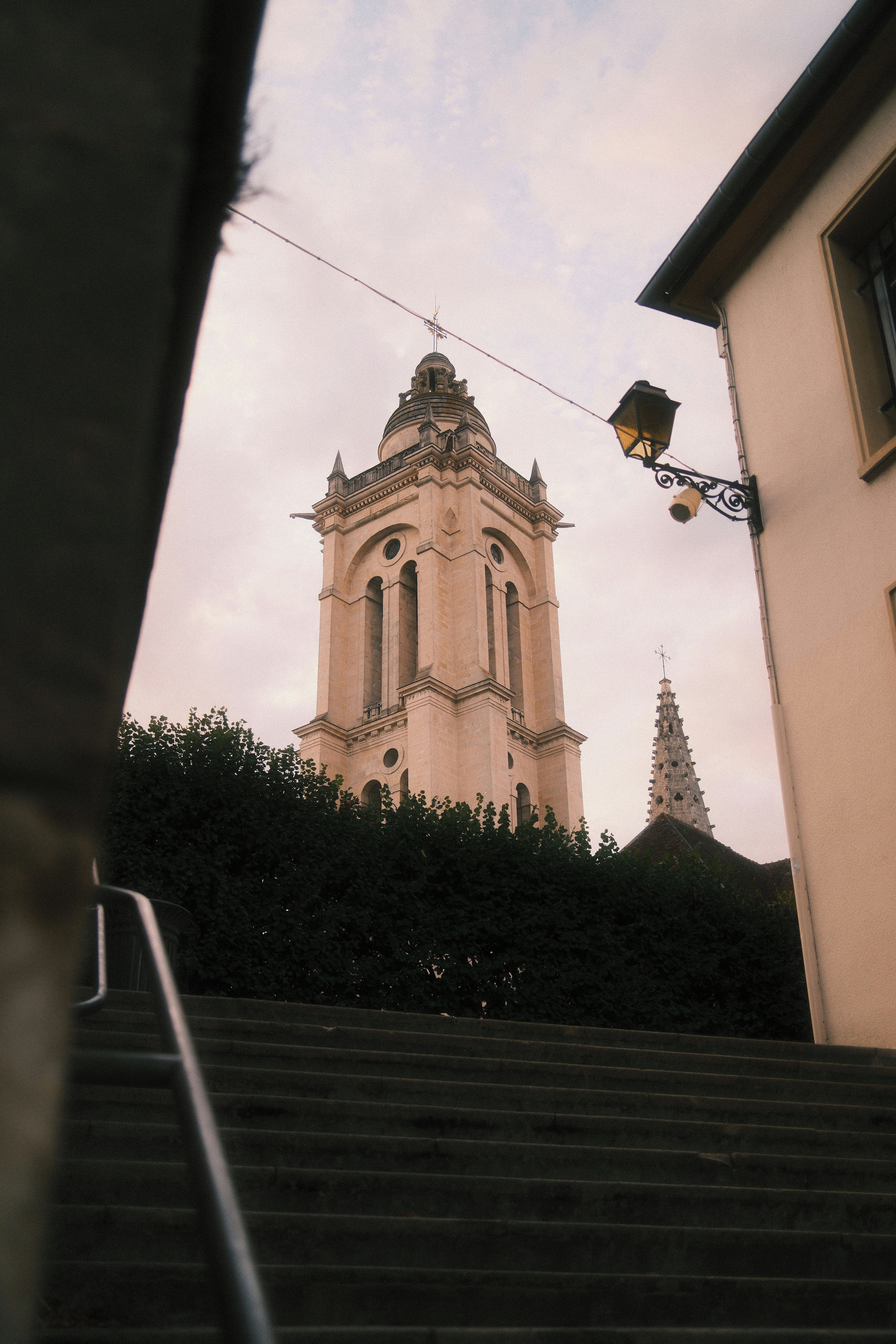 A stone church tower rising above a hedge at the top of stairs