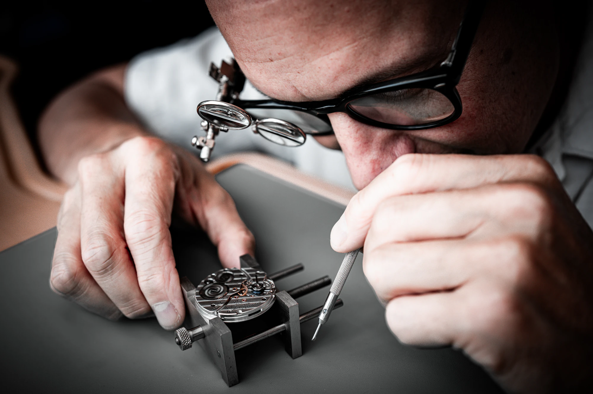 A watchmaker servicing a movement with precision tools at the bench