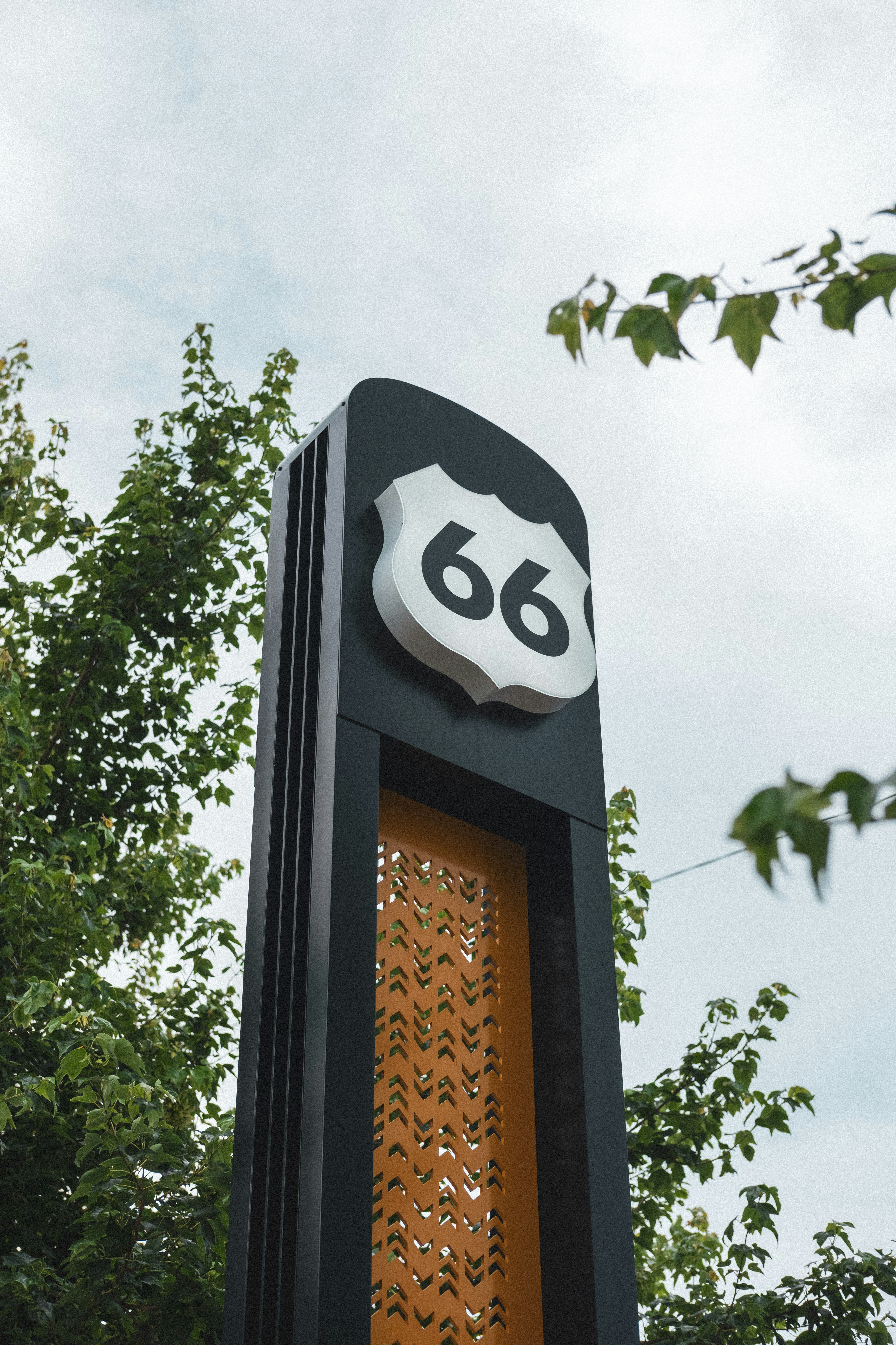 A black Route 66 sign on a tall post among green tree branches