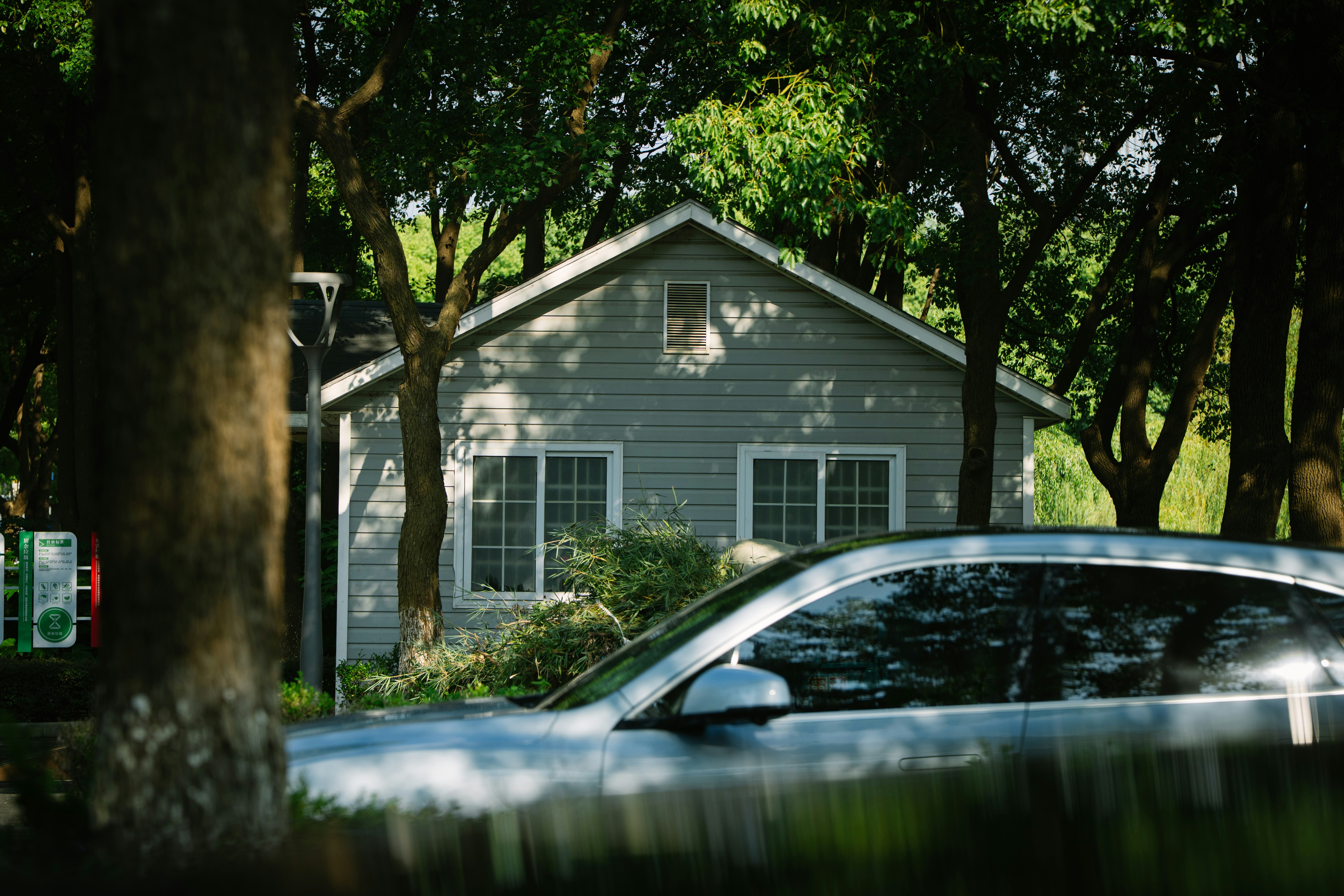A grey house with white trim nestled among dense green trees in a park