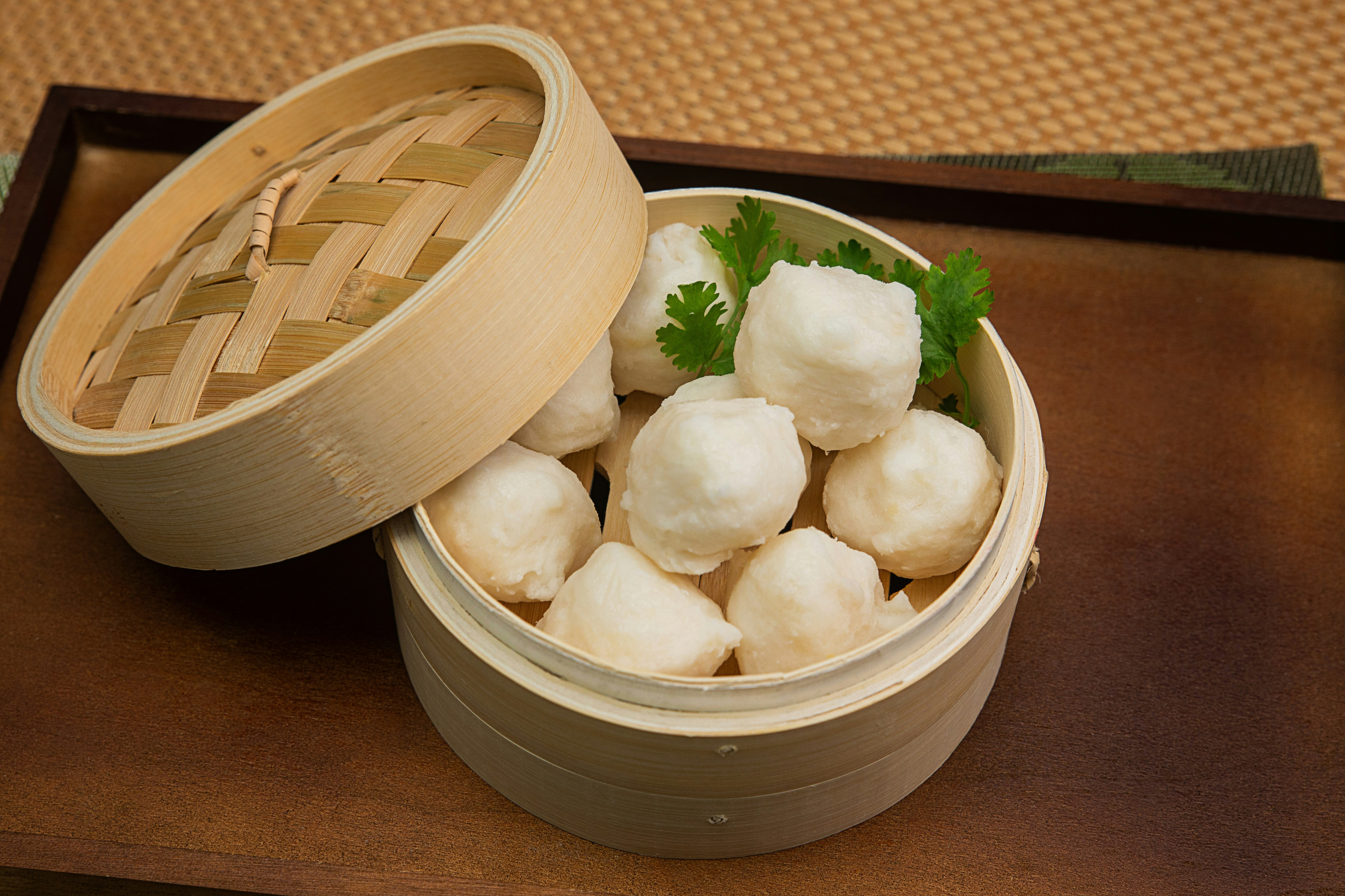 White fish balls in a bamboo steamer with a sprig of cilantro