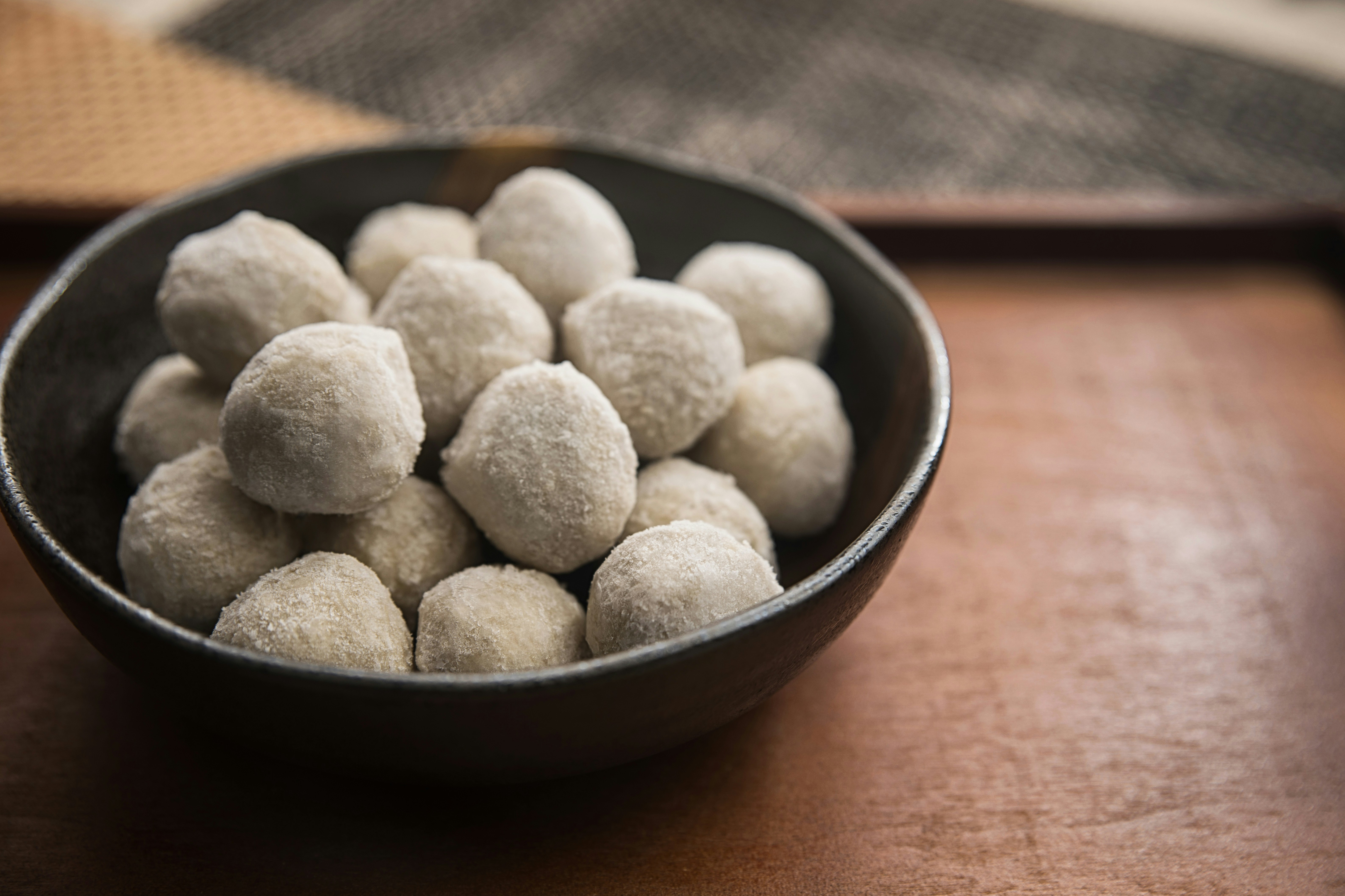 A bowl of round white powdered cookies on a wooden tray