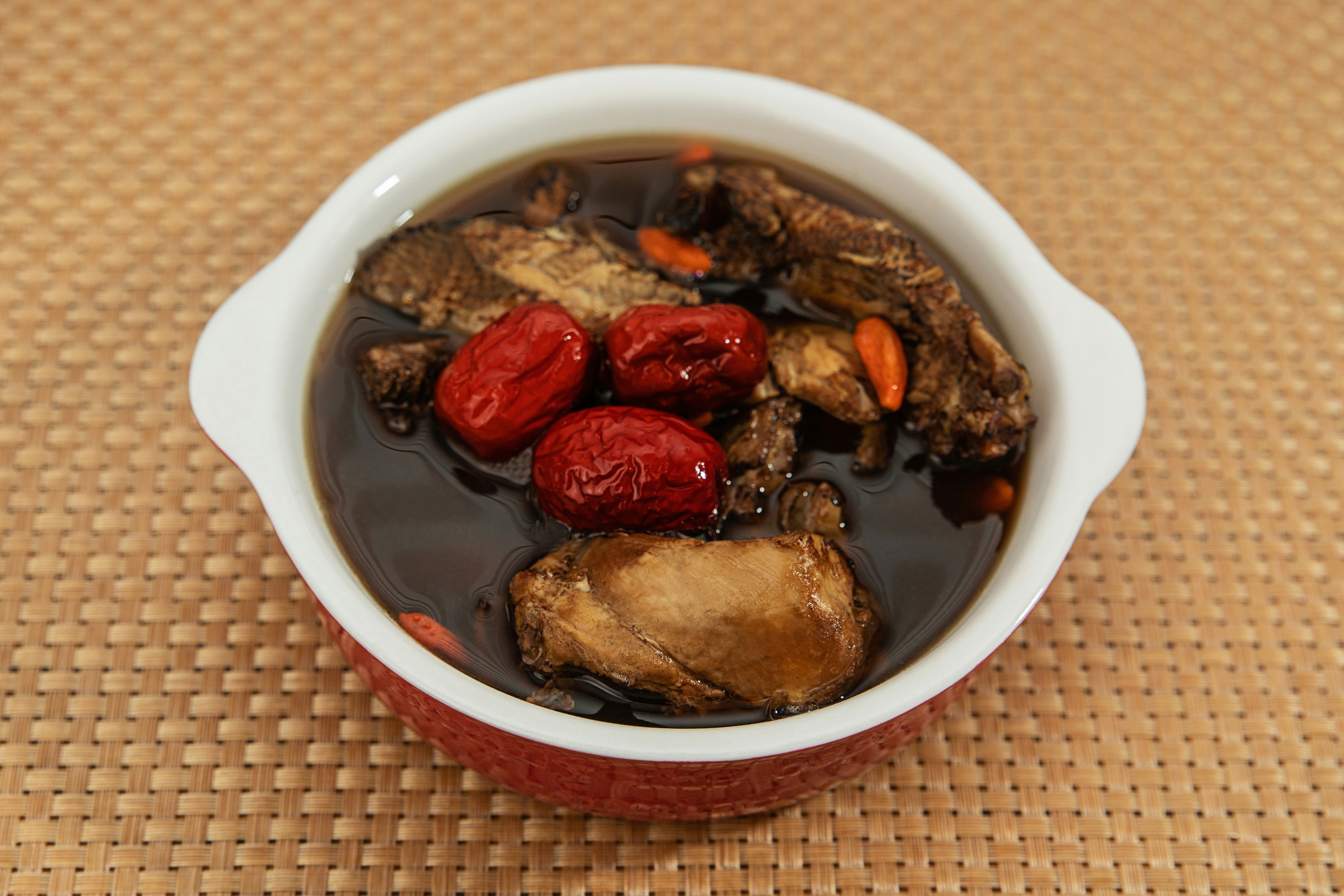 A bowl of dark herbal soup with chicken, red dates, and goji berries