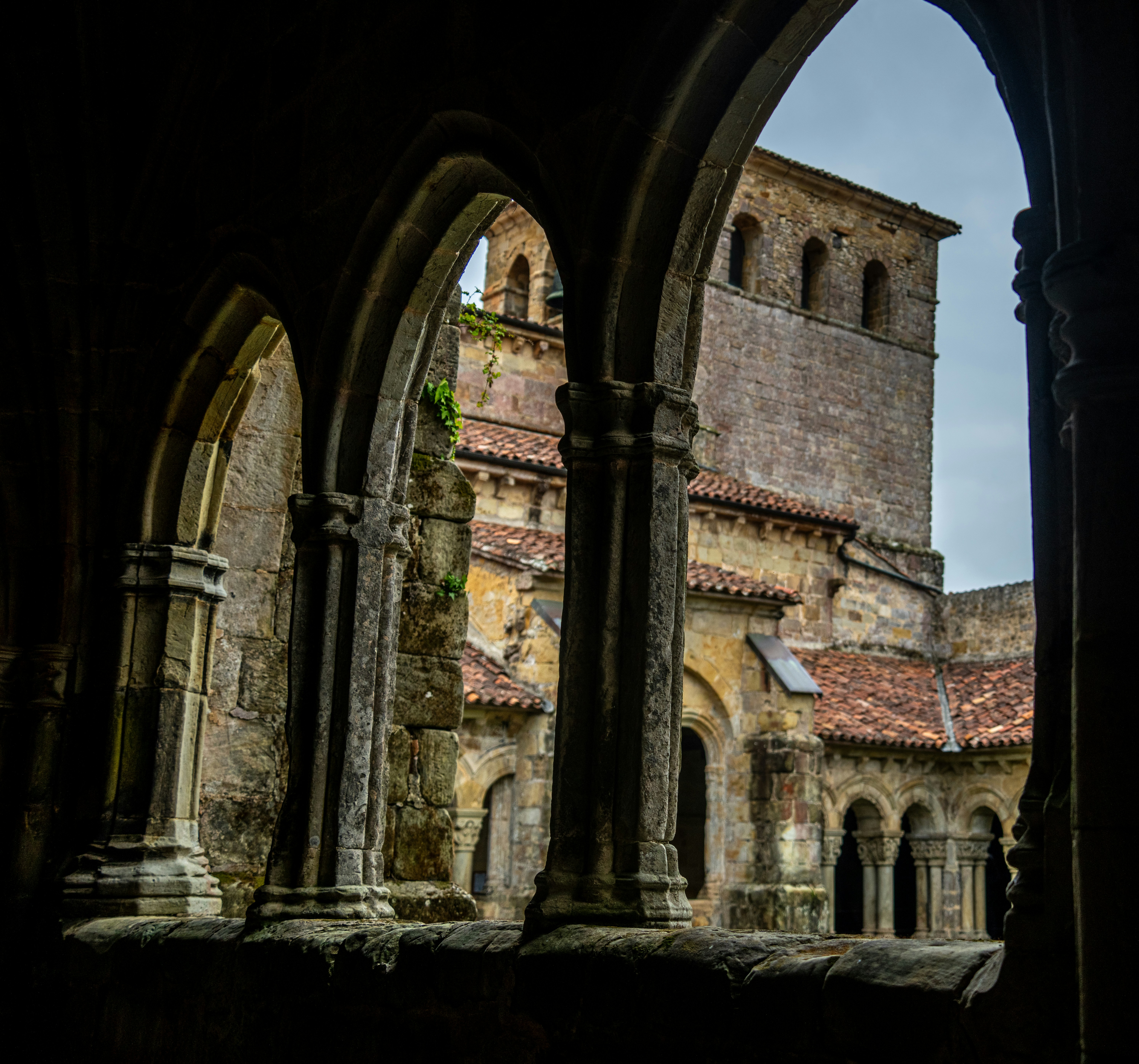 Stone arches framing a view of a medieval monastery courtyard with tiled roofs
