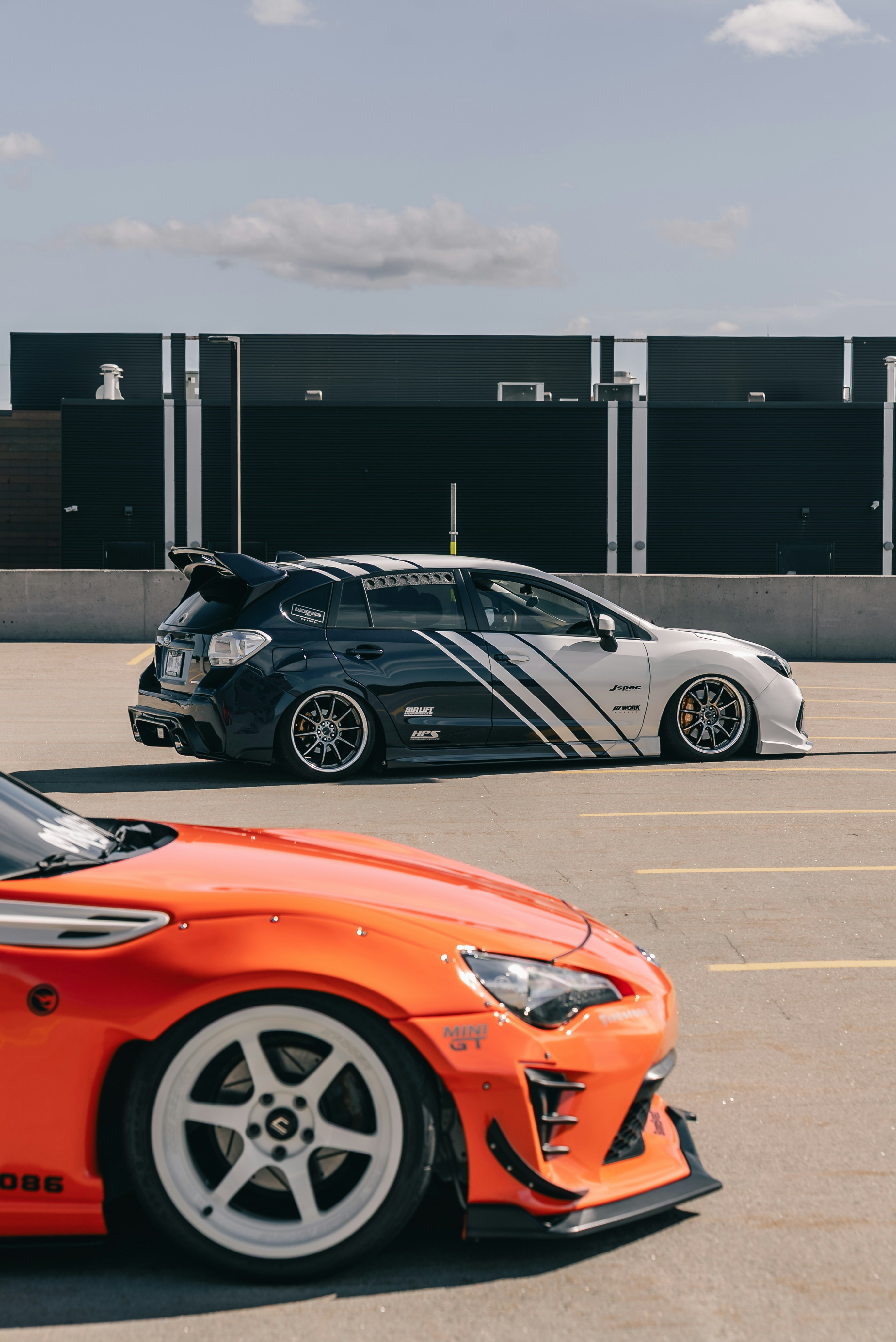 A modified orange sports car in the foreground and a black and white hatchback