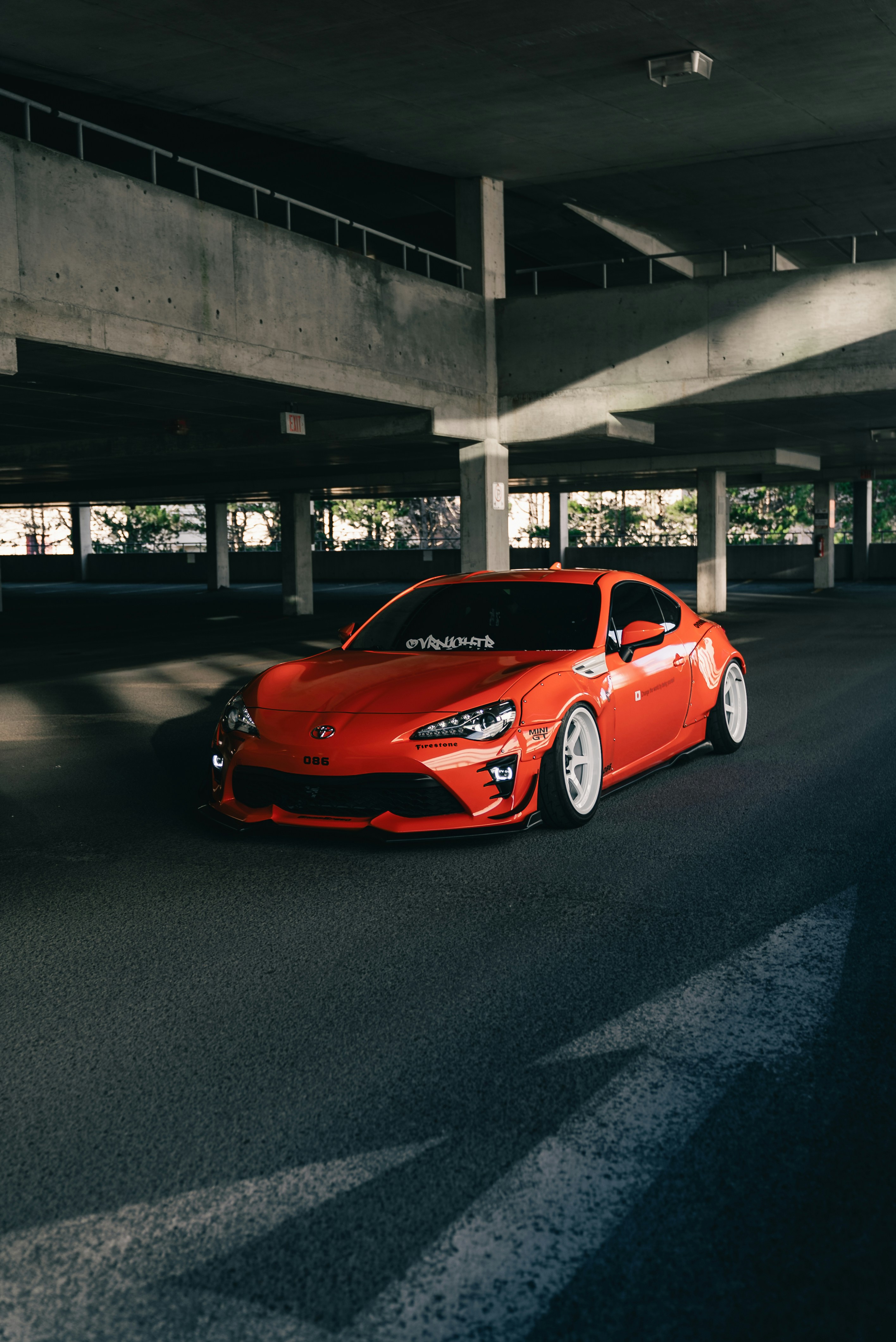 An orange Toyota 86 sports car with white wheels in a concrete parking garage