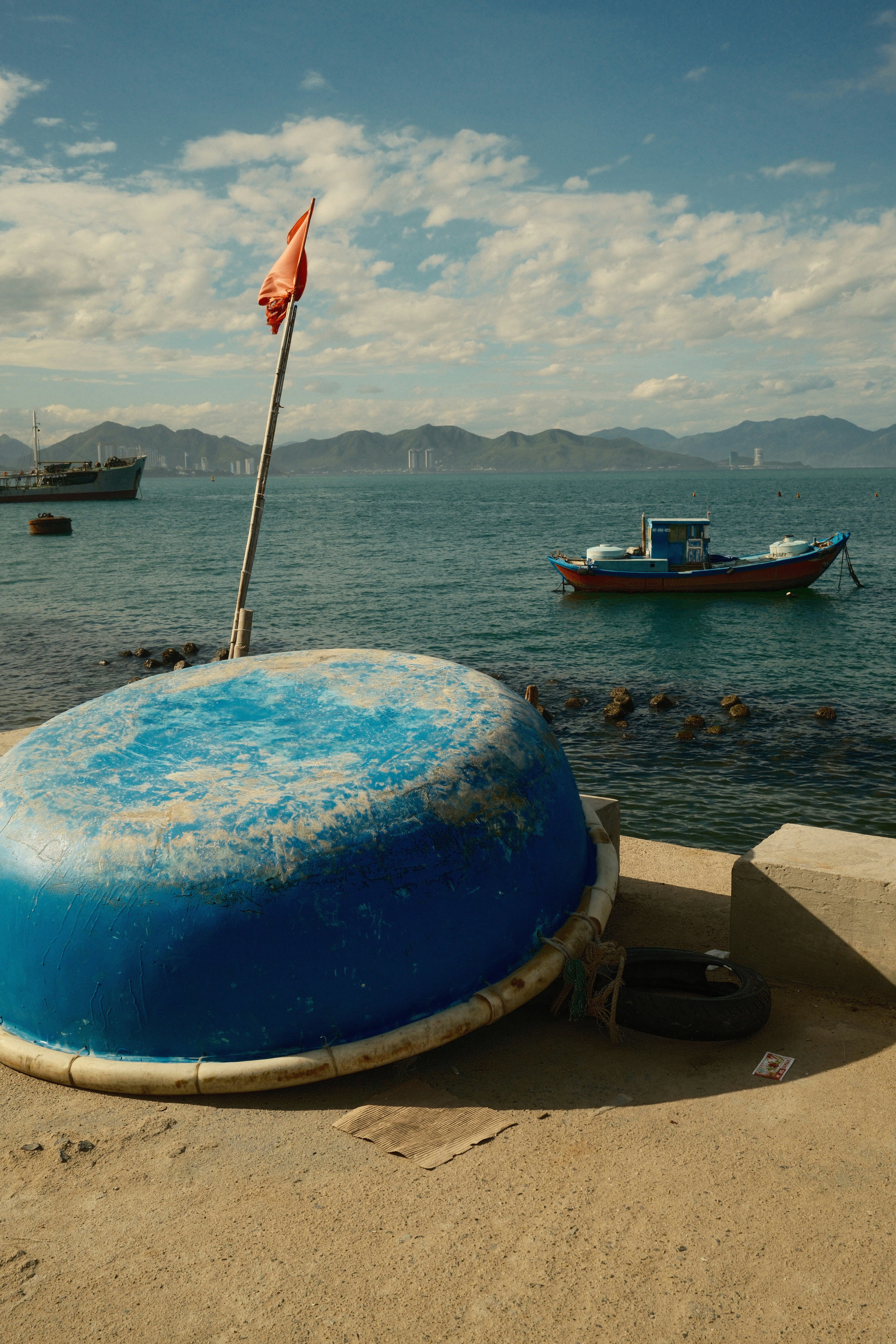Ein blaues rundes Korbboot auf einem Betonpier mit einem Fischerboot vor der Küste