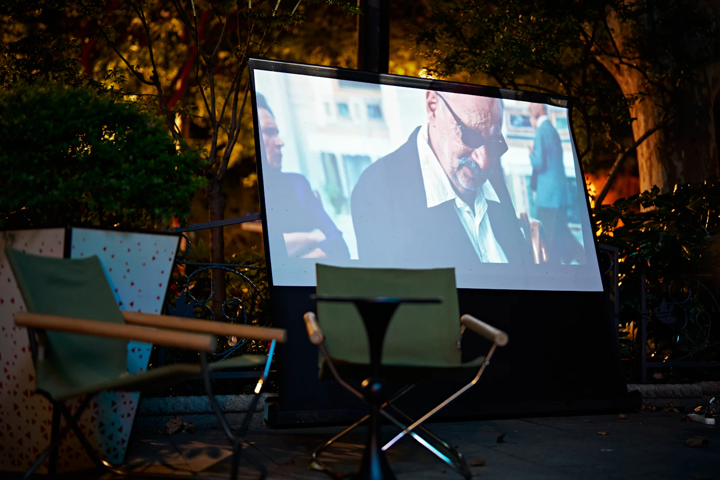 A portable projector screen showing a film in a garden with two chairs in front of it