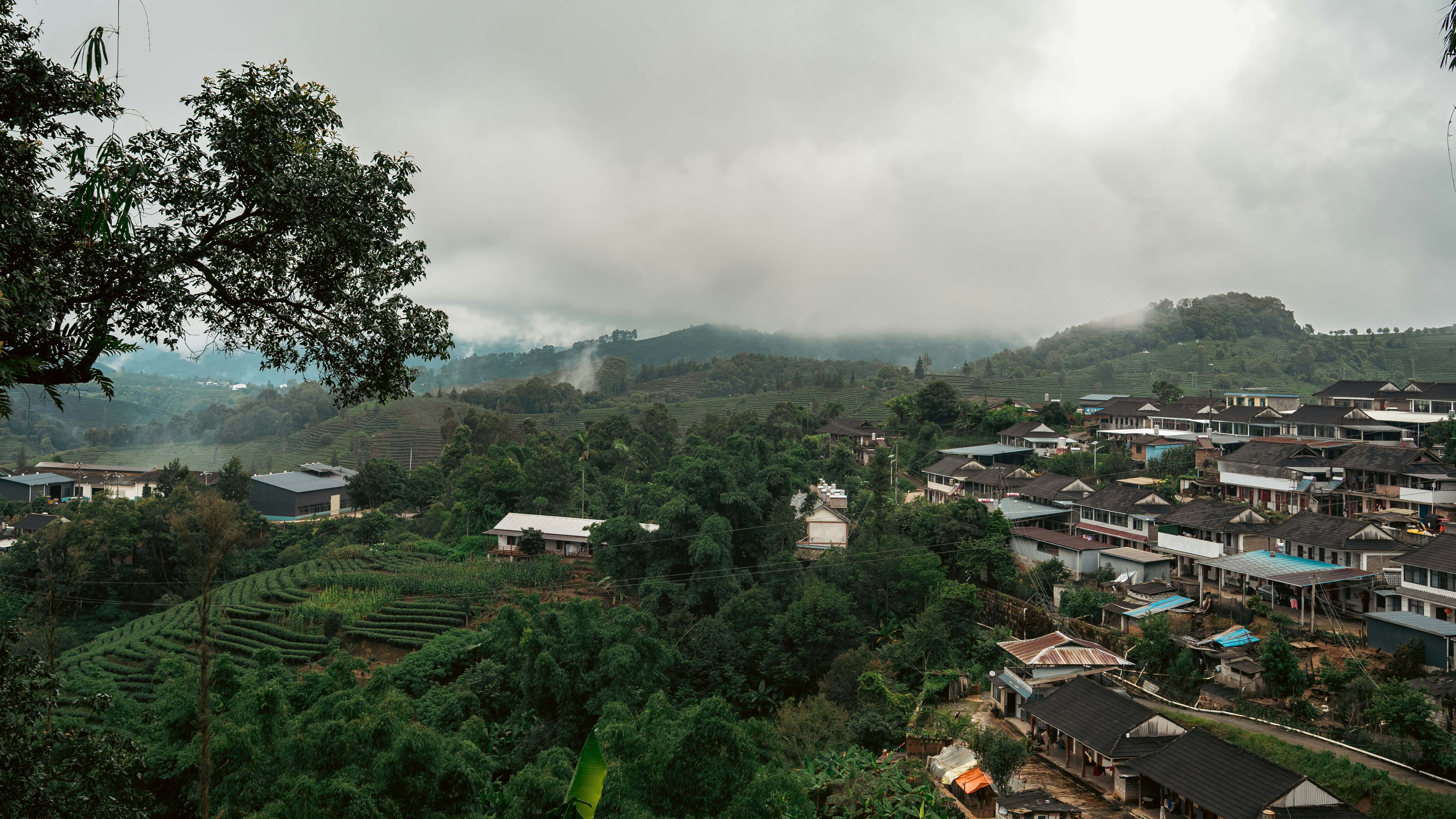 A village nestled in a green valley with terraced fields under a cloudy sky