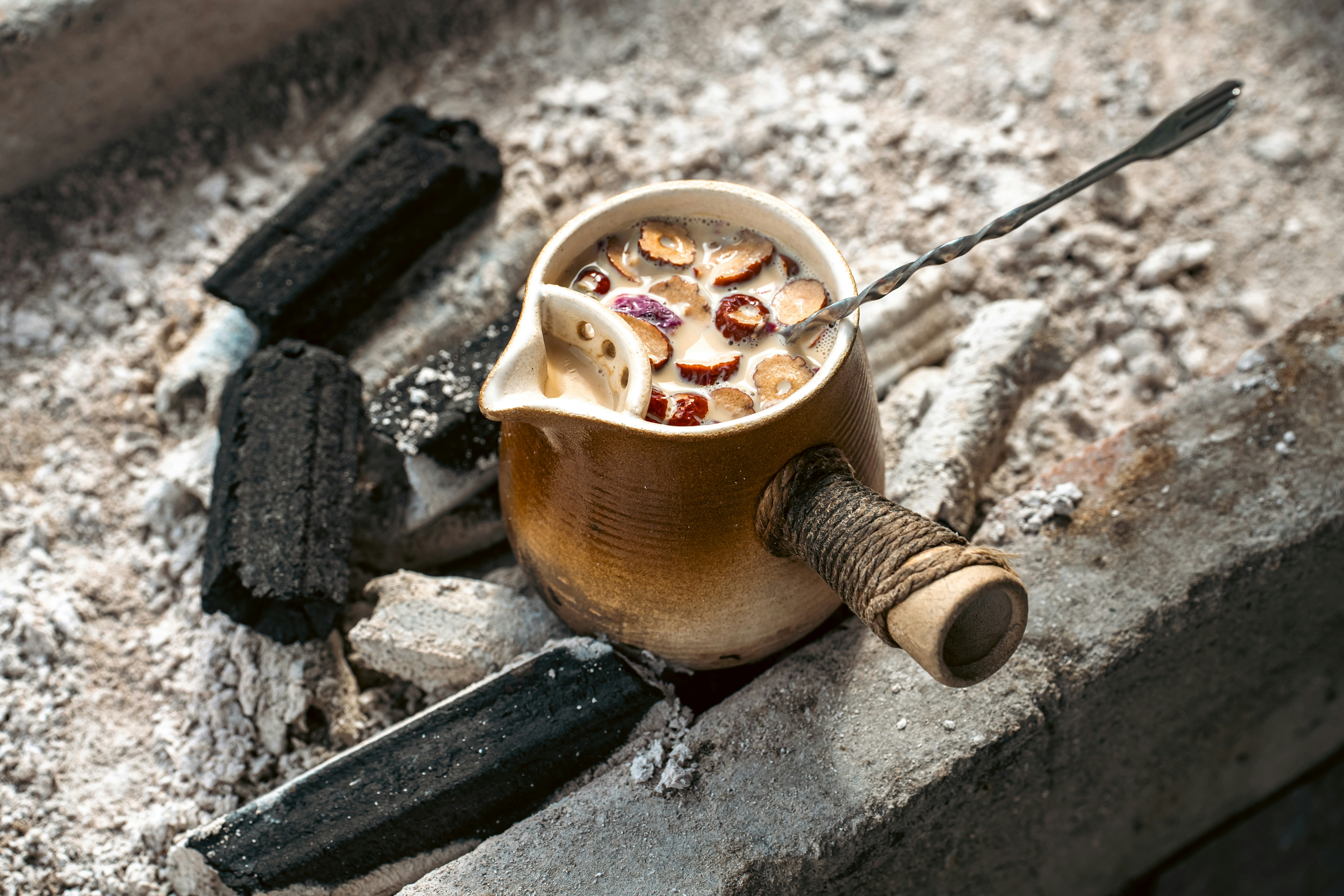 A ceramic pot of tea with sliced red dates on hot charcoal embers