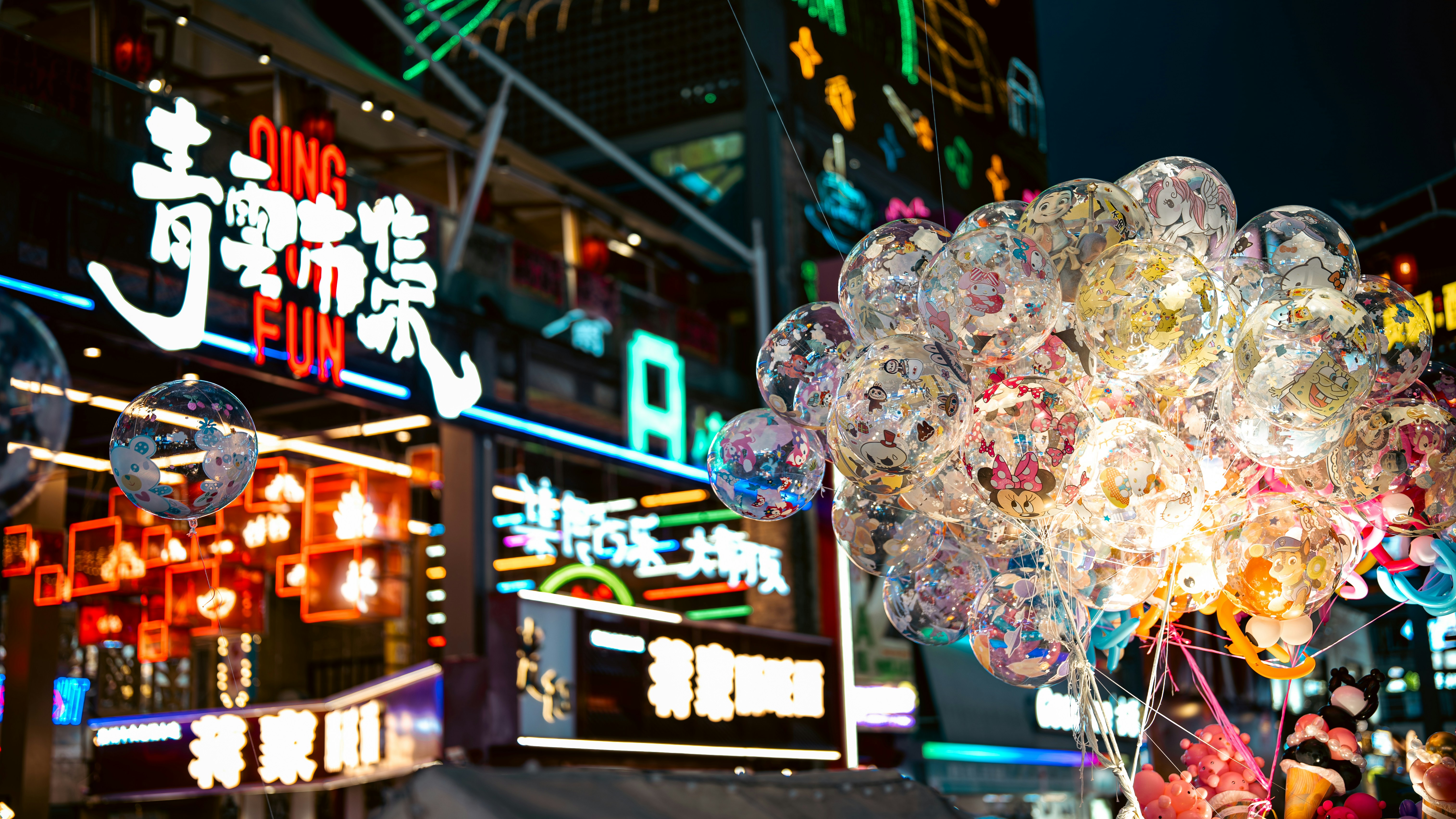 A cluster of clear balloons with cartoon characters against a neon-lit night market
