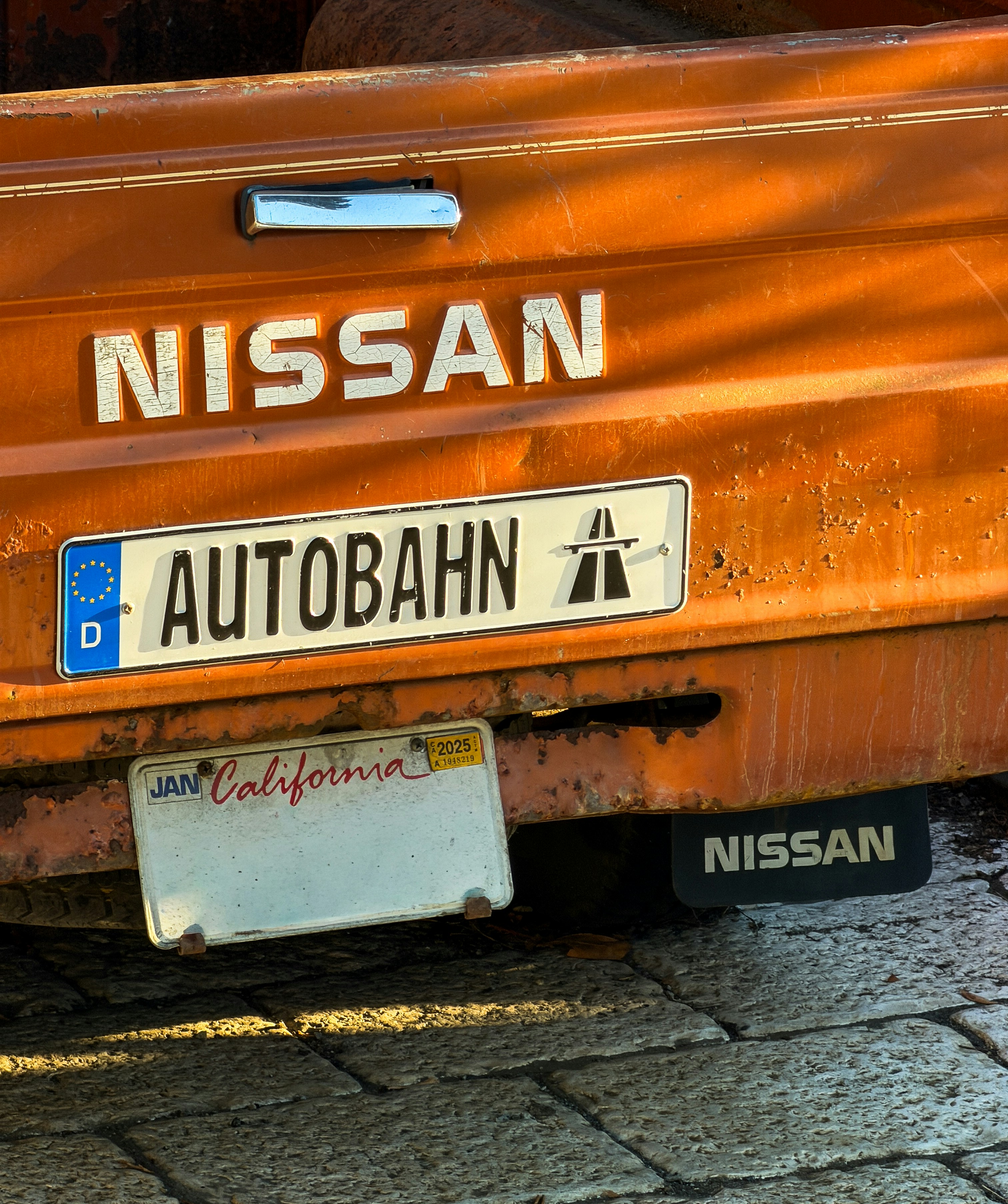 The tailgate of an orange Nissan truck with a California license plate