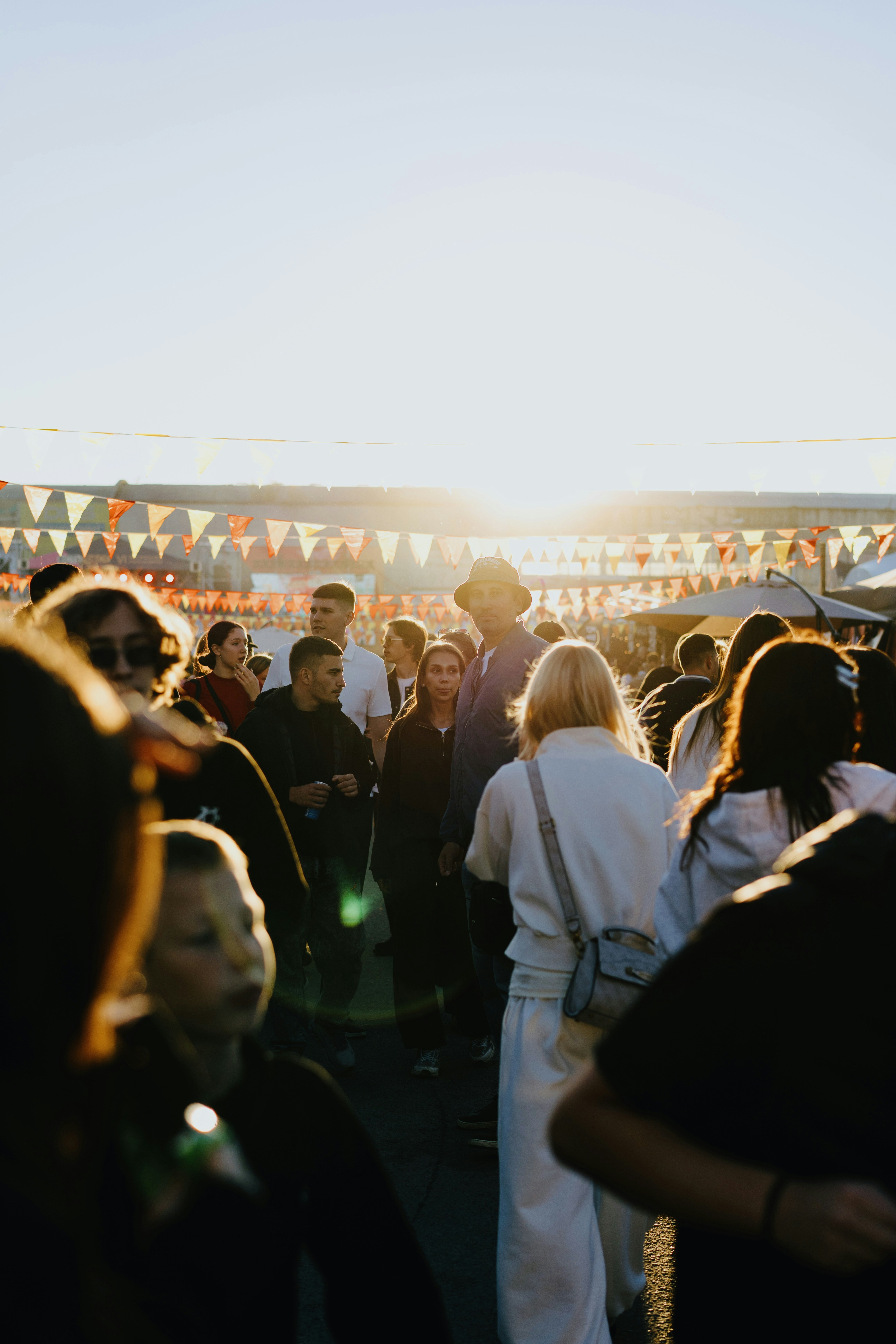 A crowd of people at an outdoor festival under orange bunting in low sun