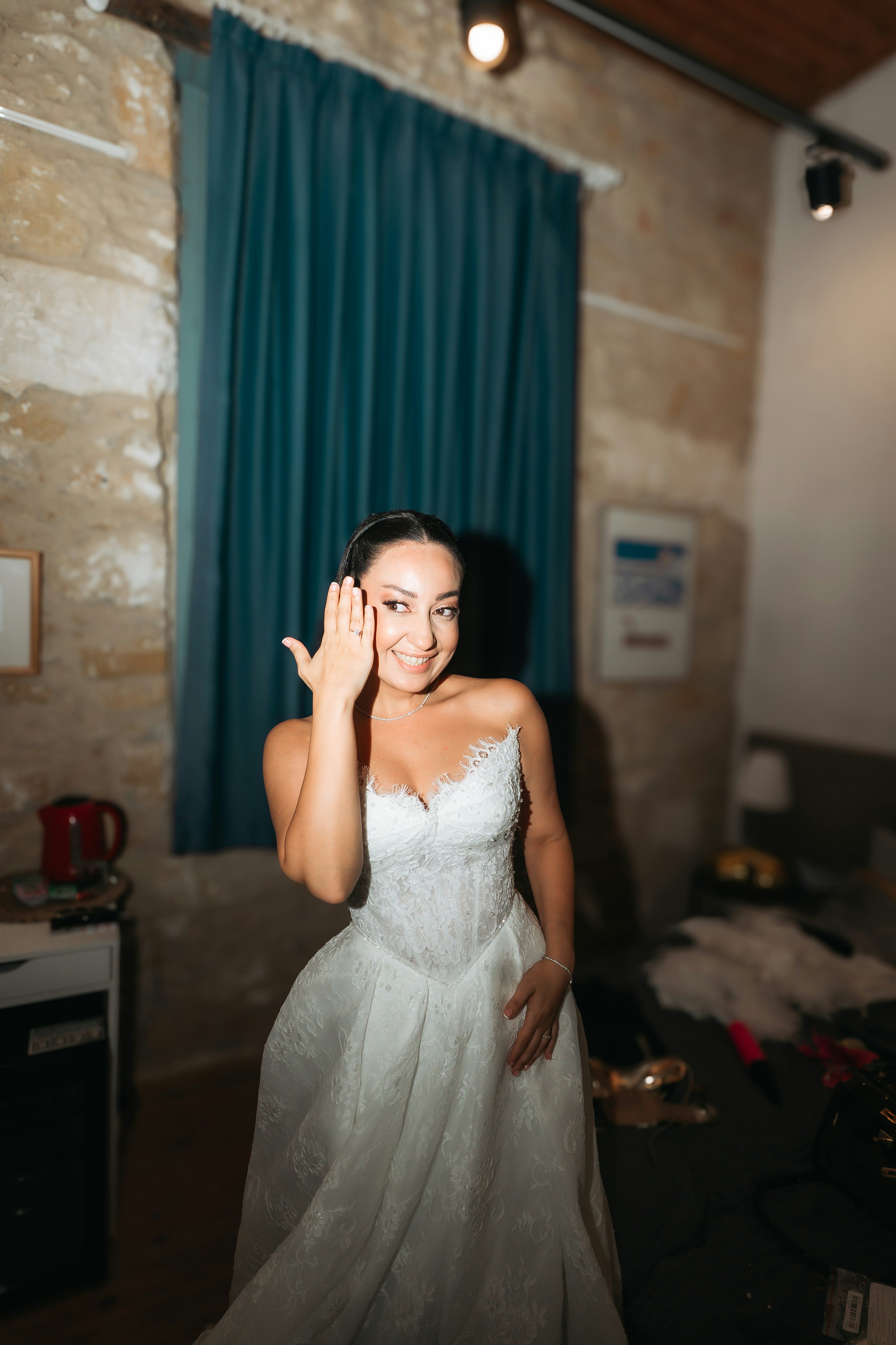 A woman in a white lace wedding dress showing her ring in a room