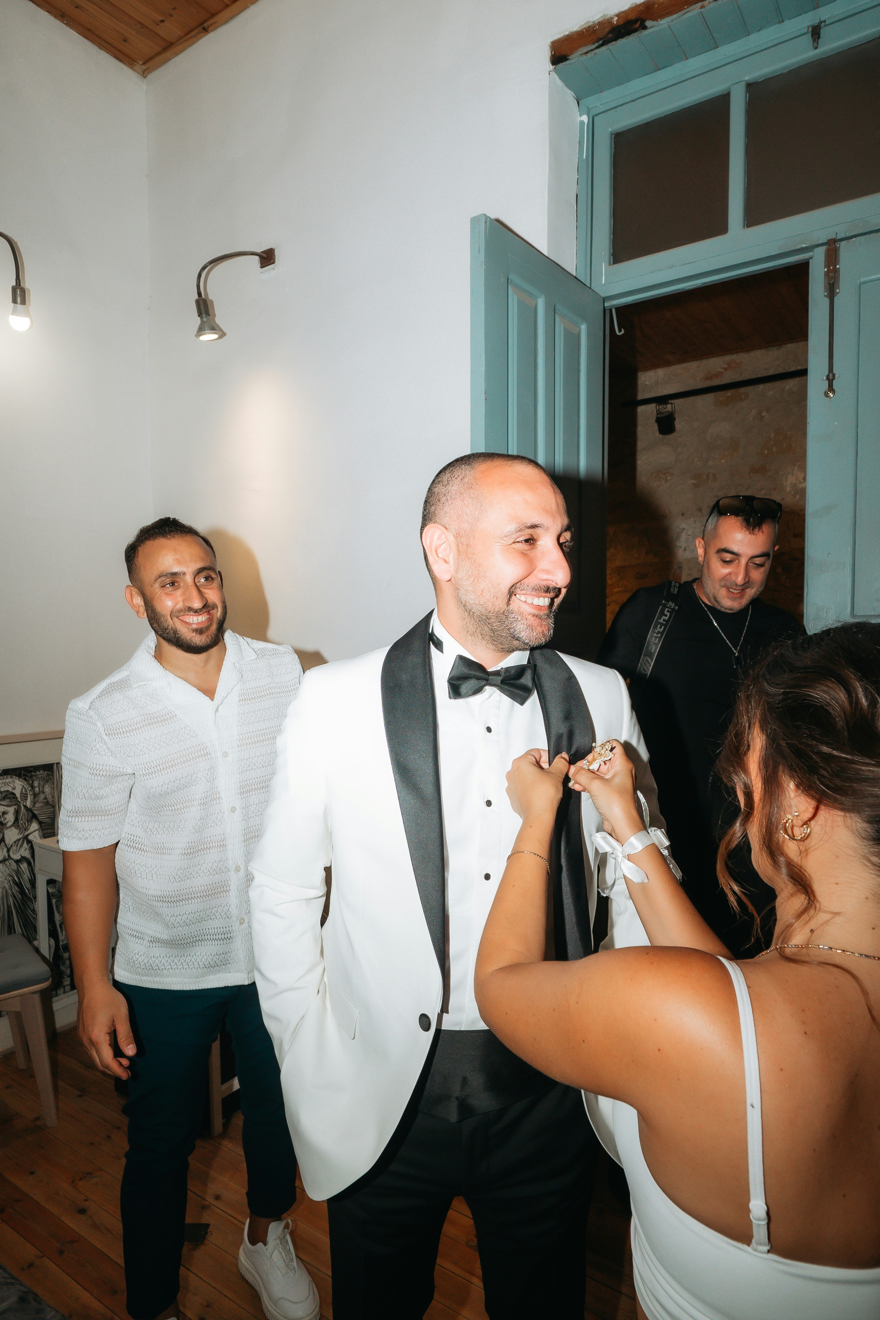 A woman pinning a boutonniere on a man in a white tuxedo jacket