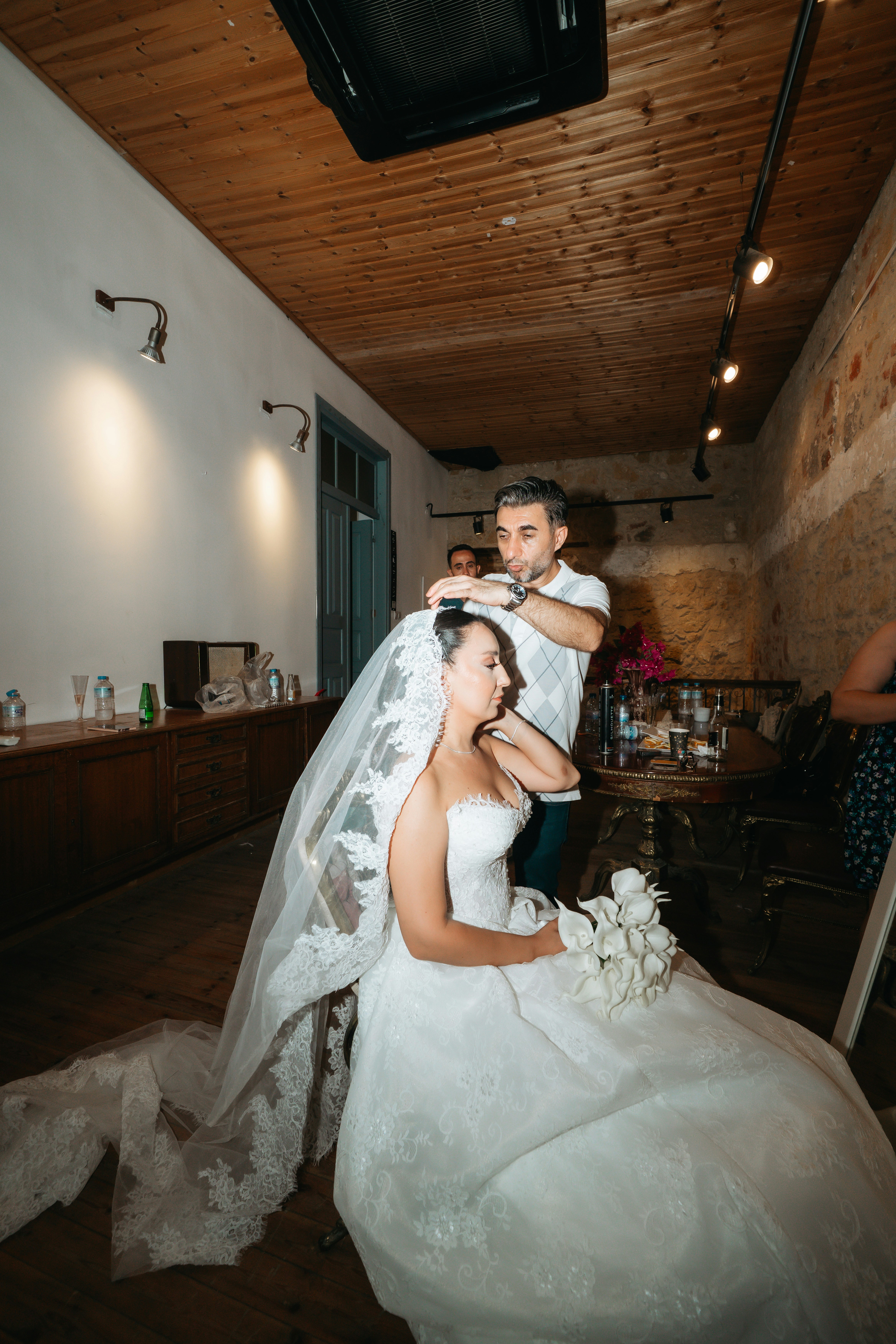 A man adjusting a lace veil on a bride in a white wedding dress