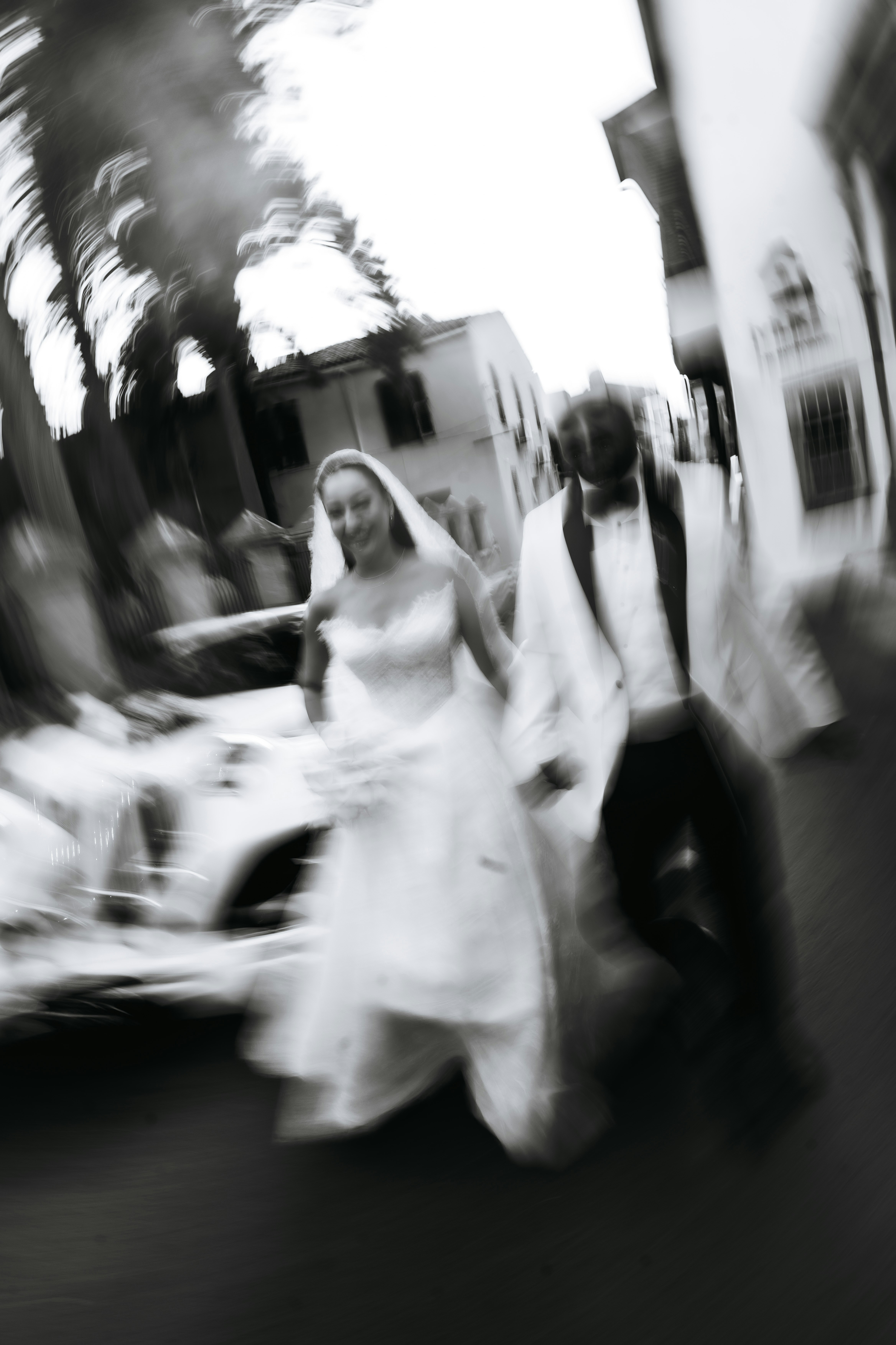 A bride and groom walking past a car in a motion-blurred street scene