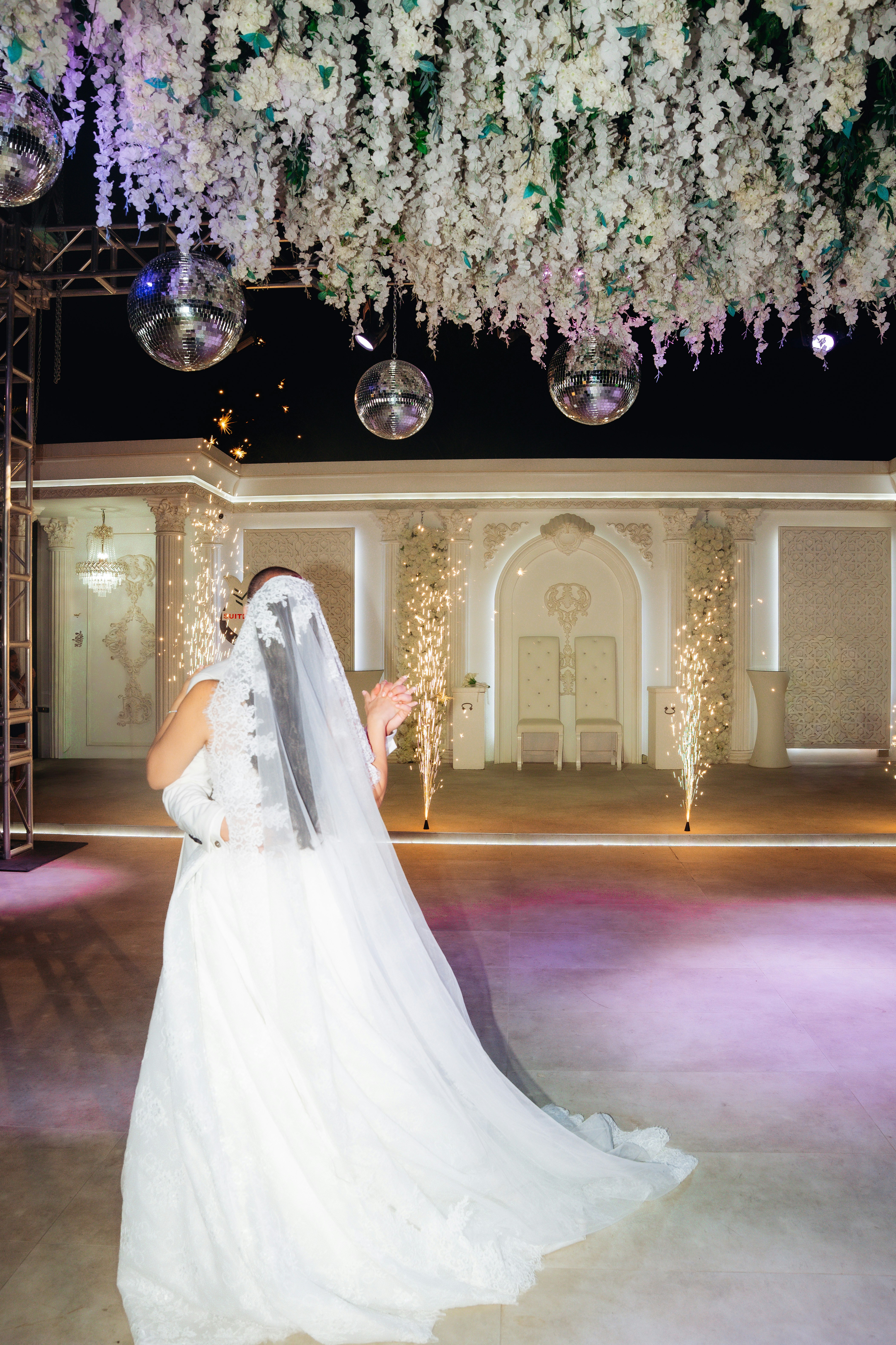 A bride and groom dancing under hanging disco balls and white floral decorations