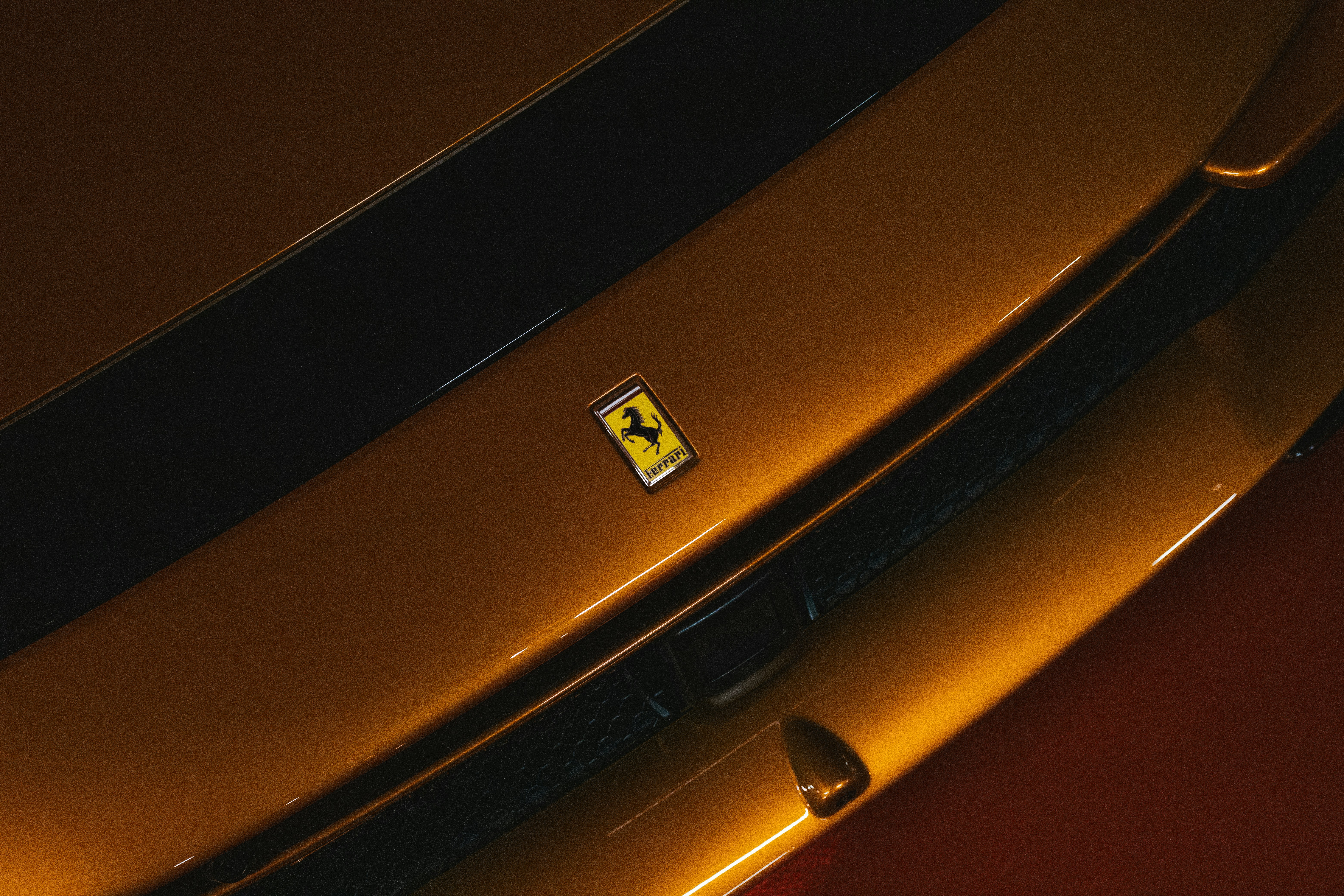A Ferrari emblem on the metallic bronze hood of a luxury sports car