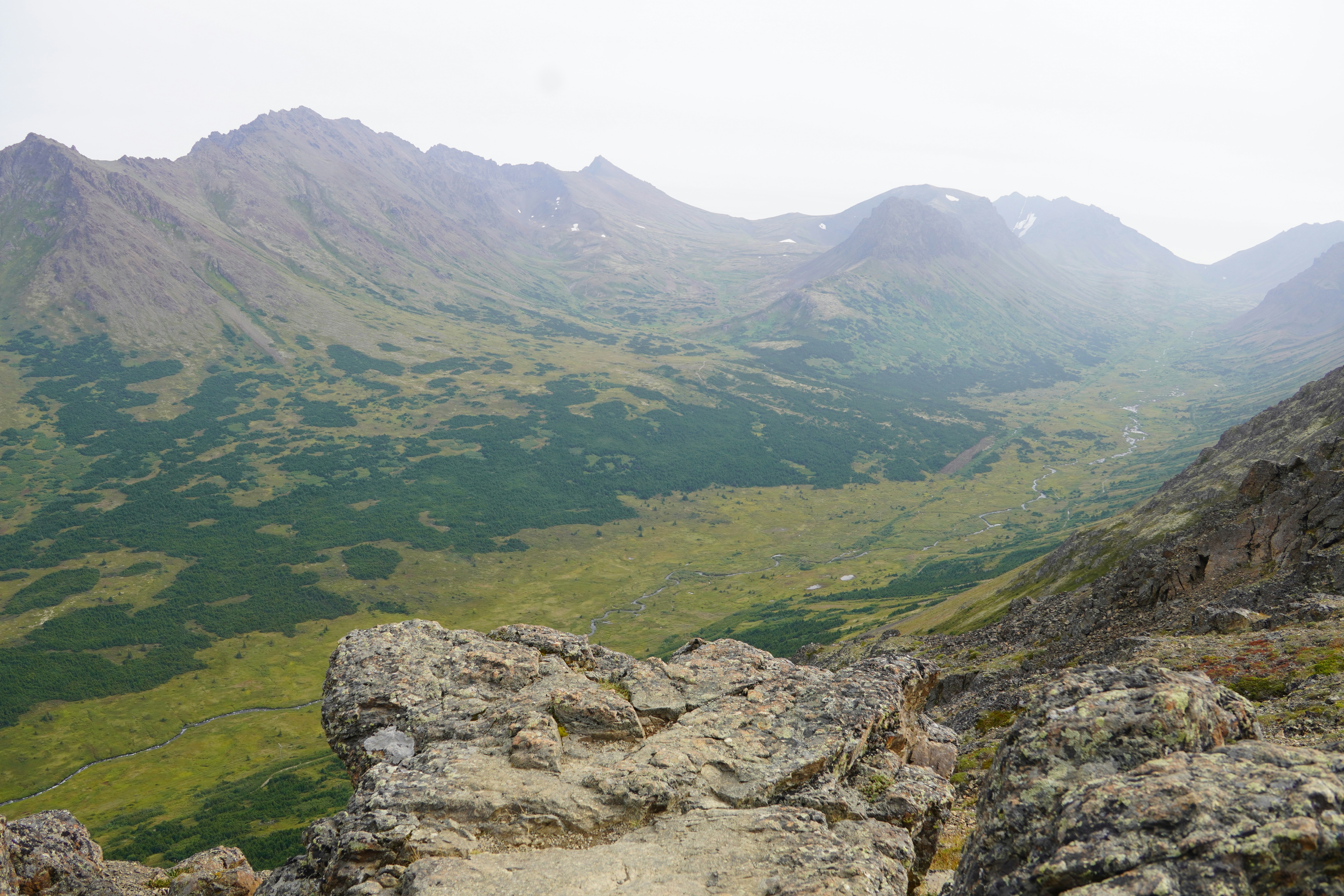 A rocky mountain overlook above a vast green valley with a winding stream
