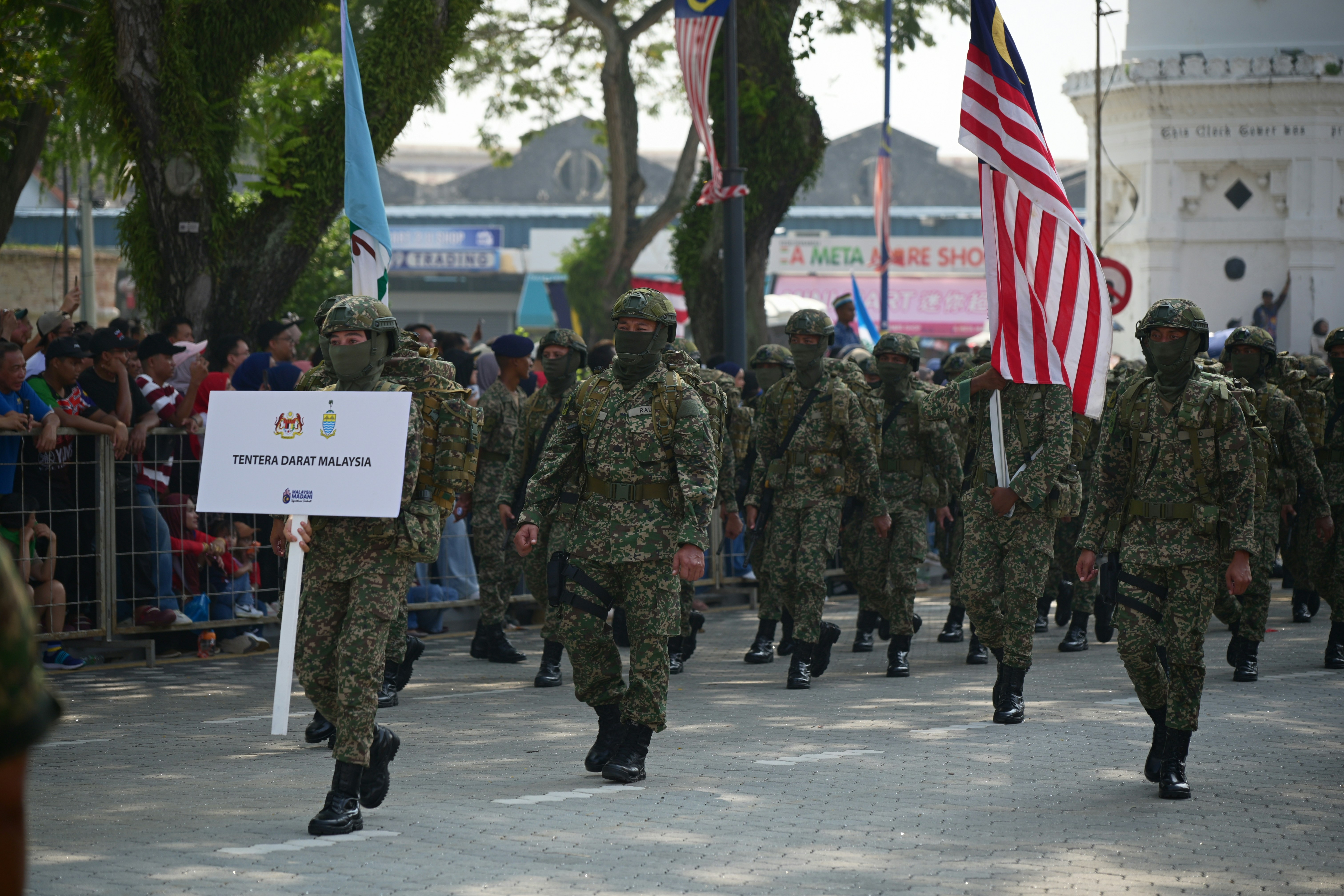 Malaysische Soldaten in Tarnuniformen marschieren in einer Parade mit einer Flagge