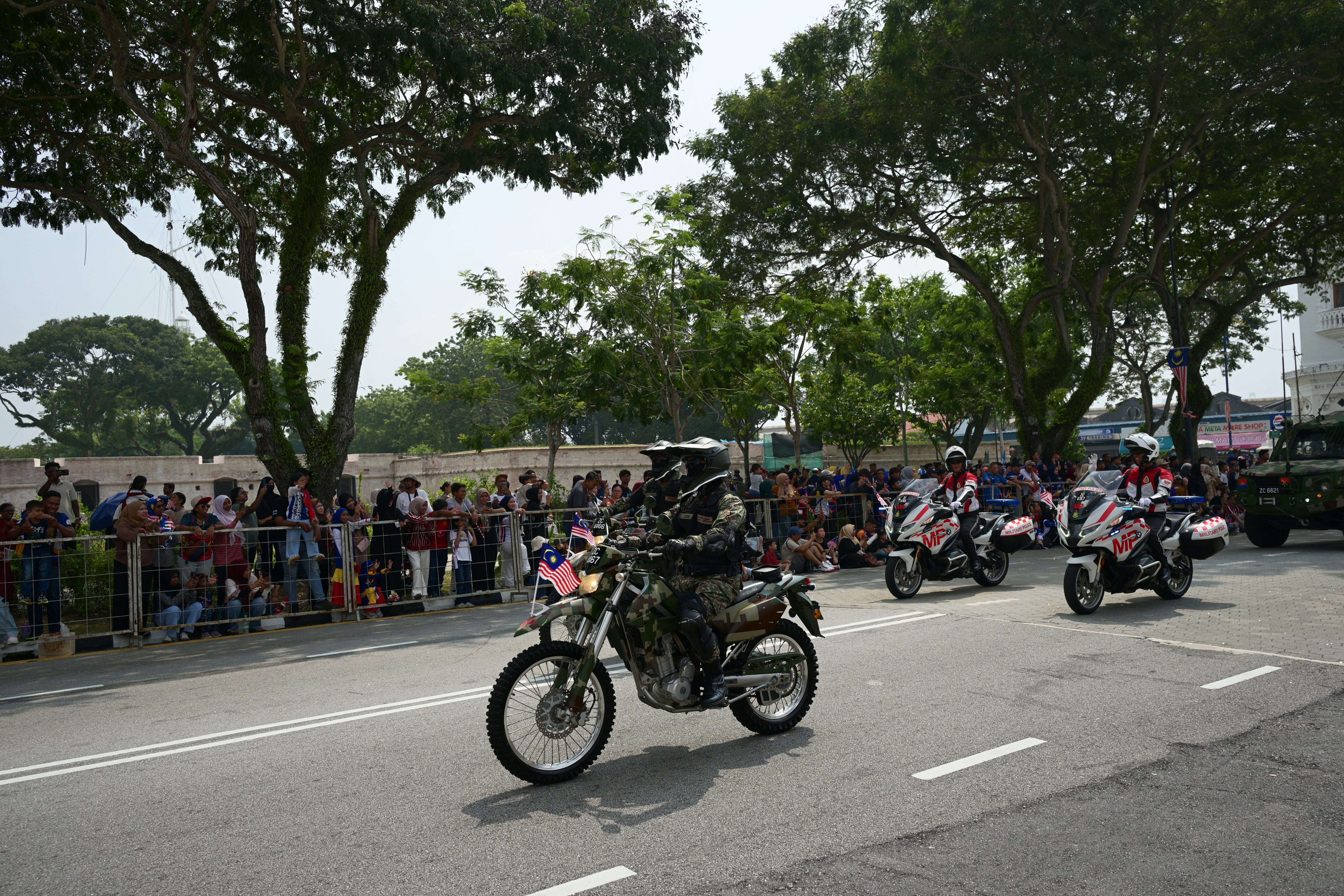 Military personnel on motorcycles riding in a parade past a crowd in Malaysia